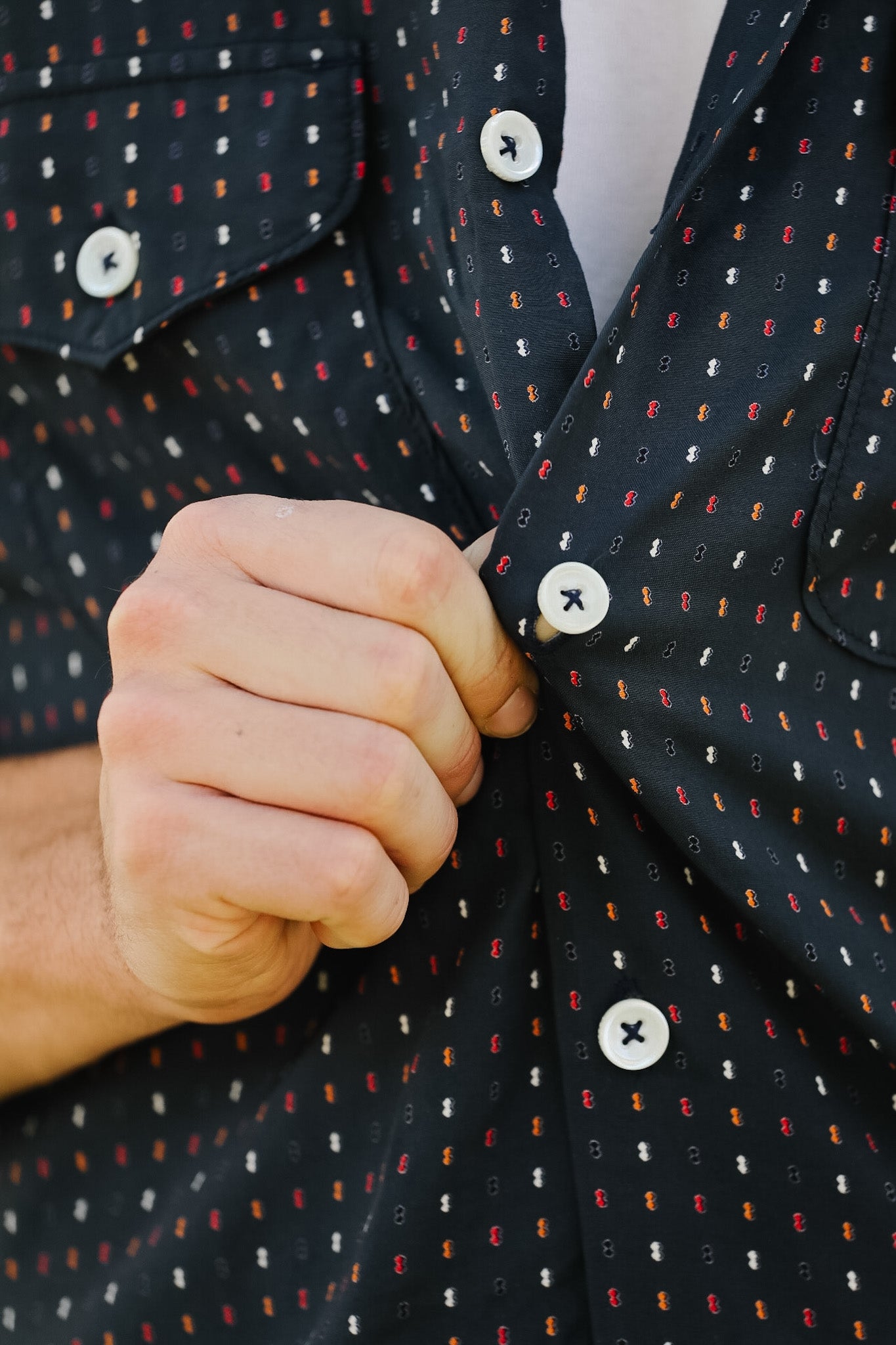 Close-up of a person buttoning a dark patterned shirt with a white button.