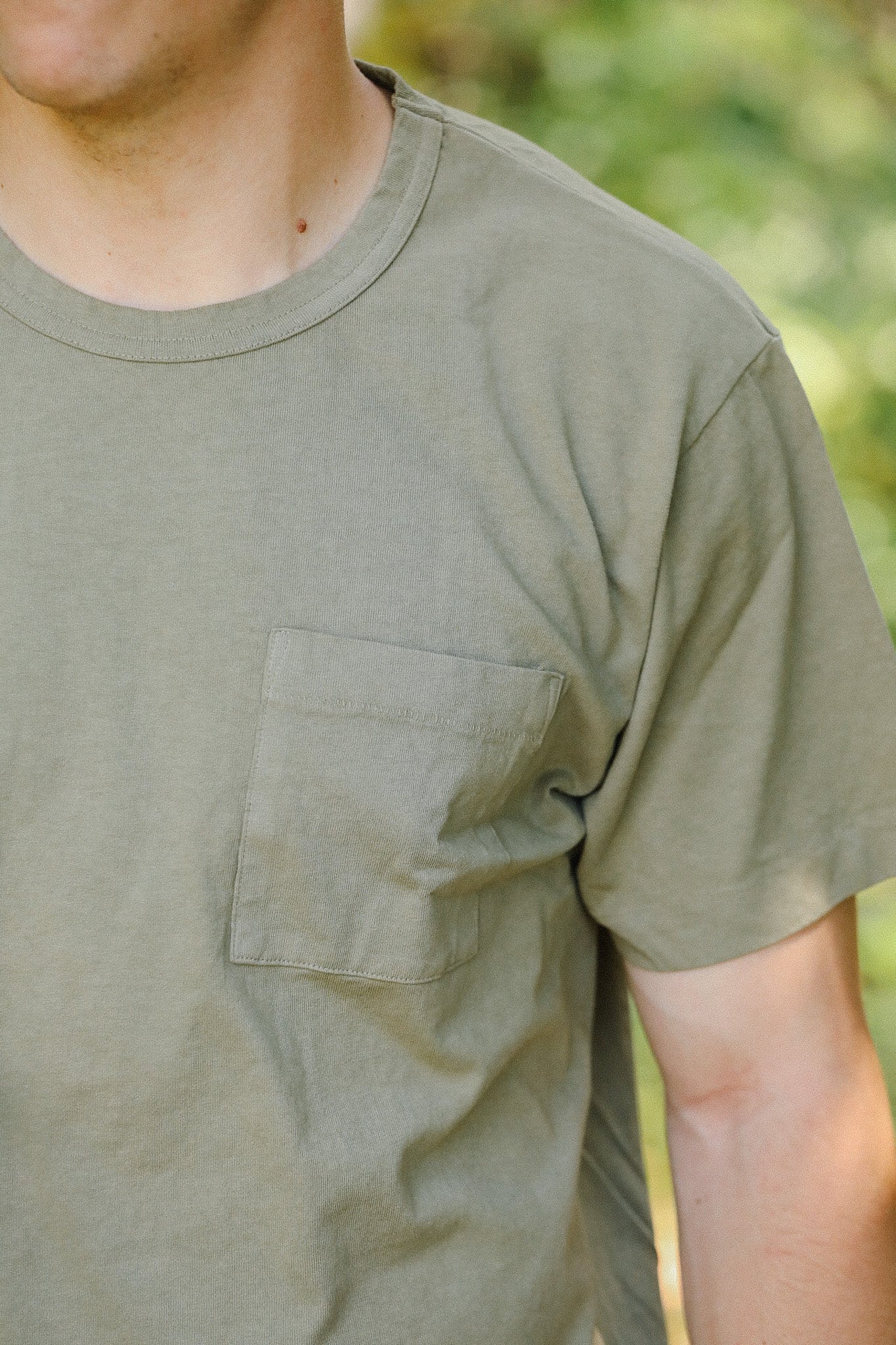 Close-up of a man wearing an olive green cotton t-shirt with a chest pocket outdoors