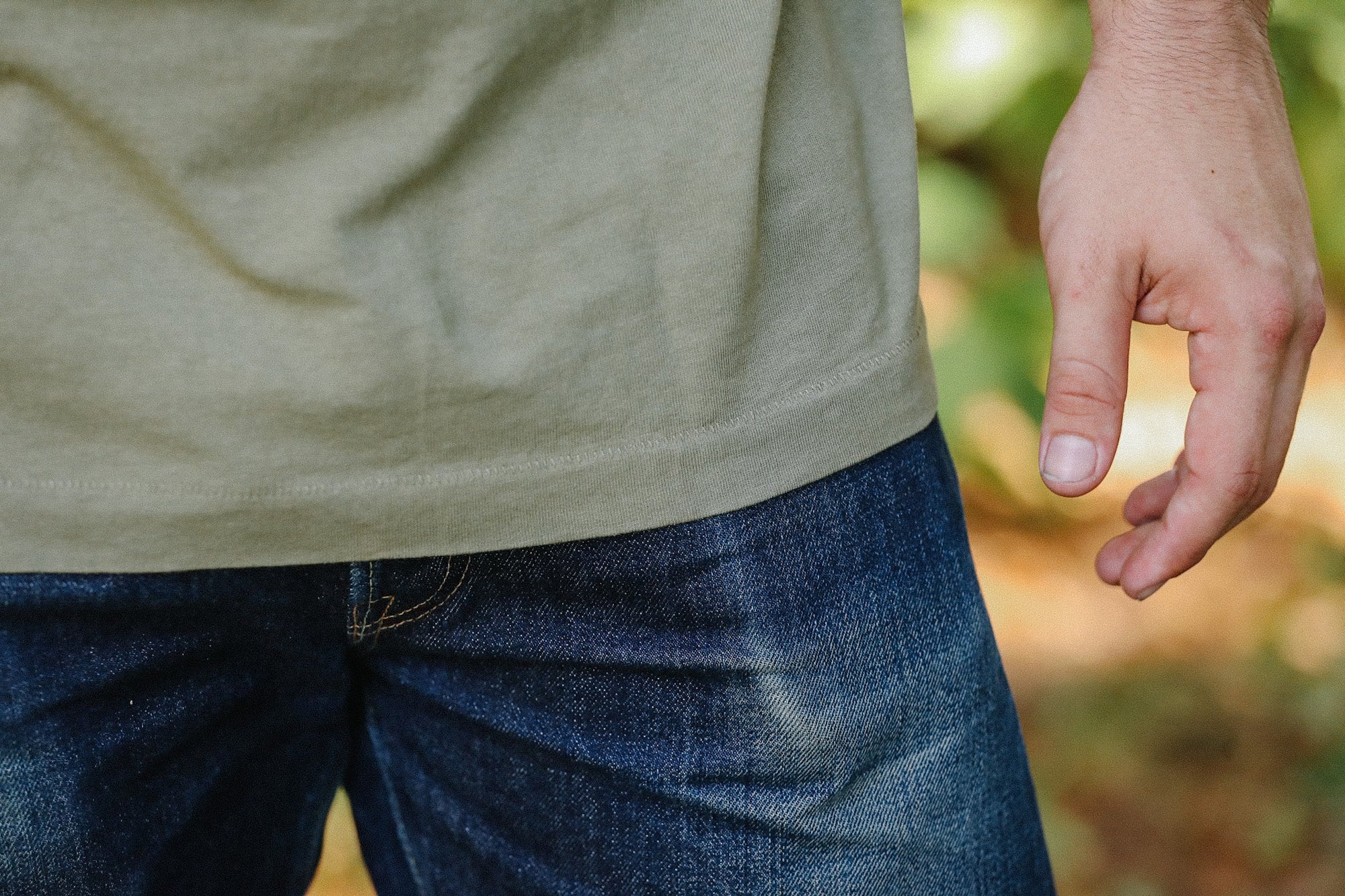 Close-up of person wearing olive green t-shirt and dark blue jeans outdoors with hand relaxed at side