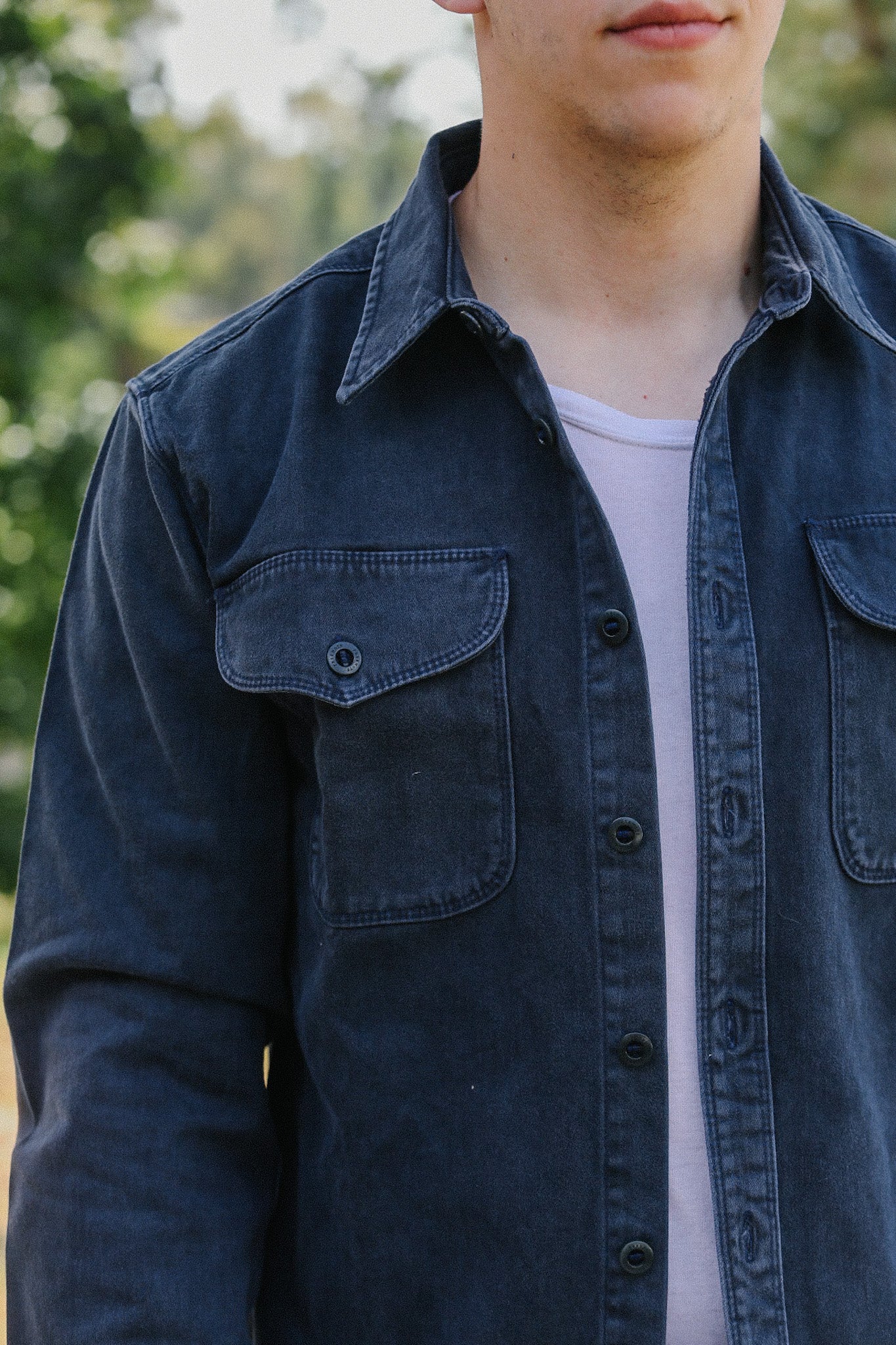Close-up of man wearing a faded black button-up shirt over a white t-shirt outdoors