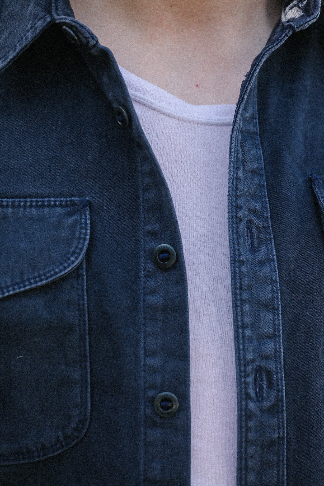 Close-up of a person wearing a dark blue denim jacket over a light gray shirt at Iron Shop Provisions