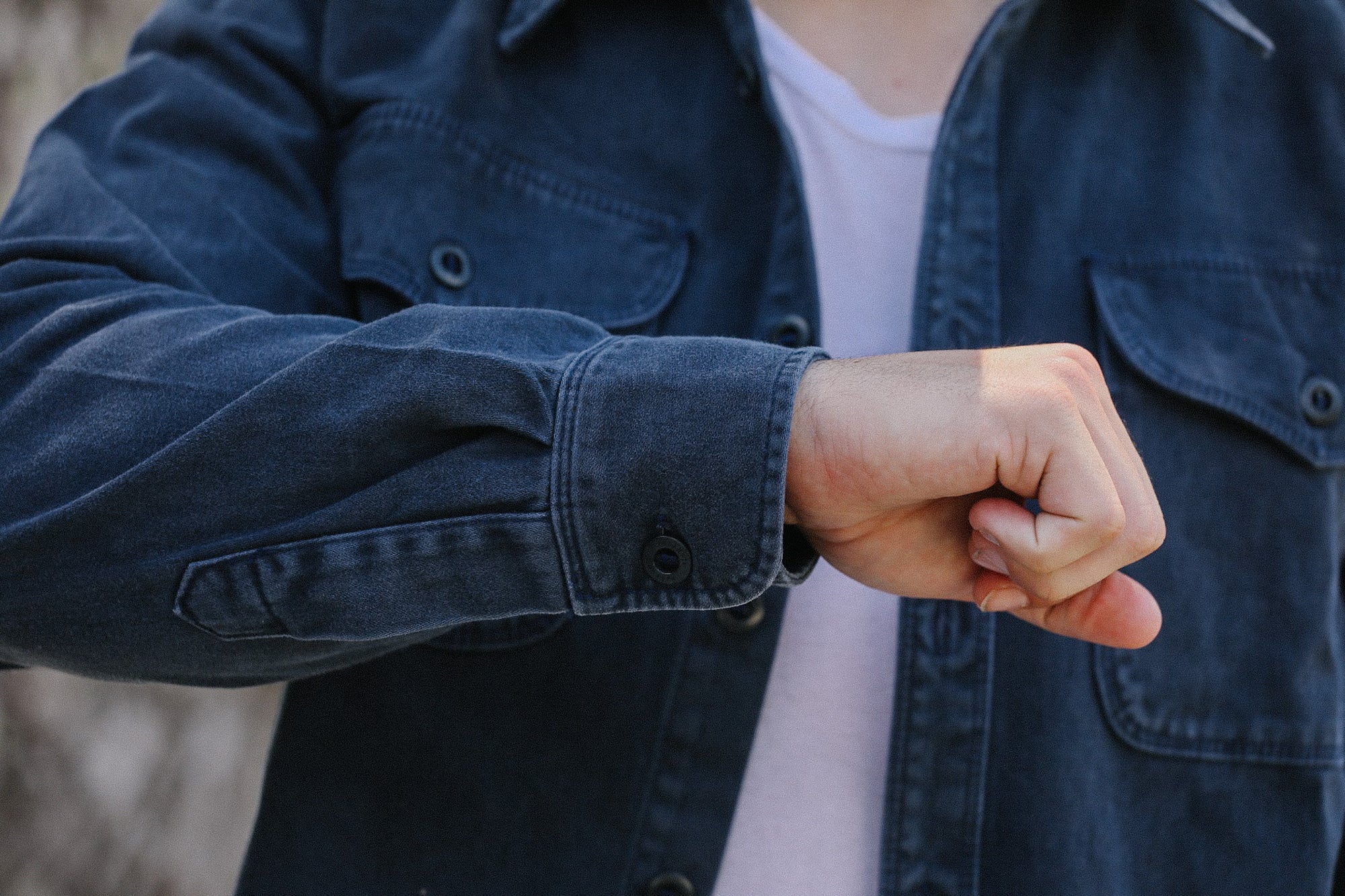 Person wearing dark denim jacket over white shirt showing clenched fist in casual outdoor setting