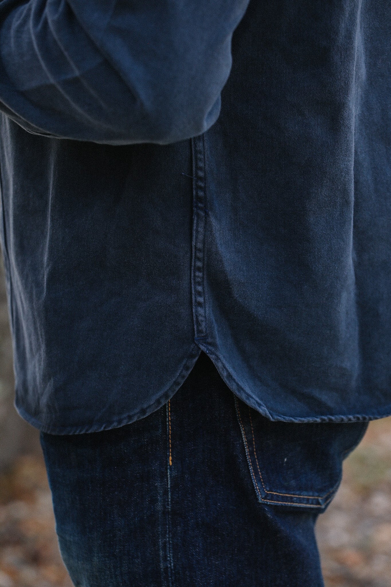 Close-up of person wearing dark blue denim shirt and dark jeans with visible stitching outdoors