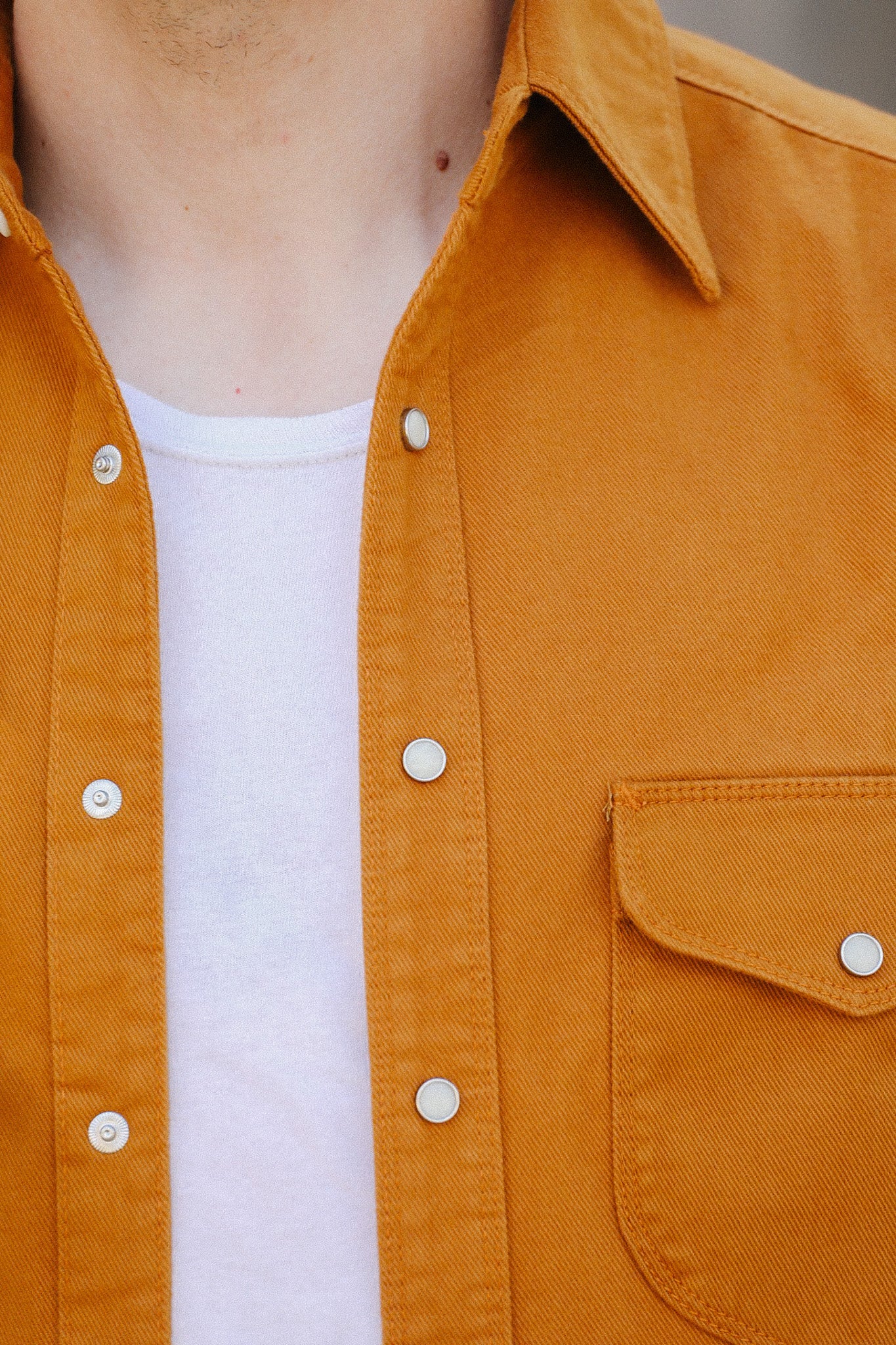 Close-up of a person wearing a white shirt under a mustard yellow button-up shirt with metal snap buttons