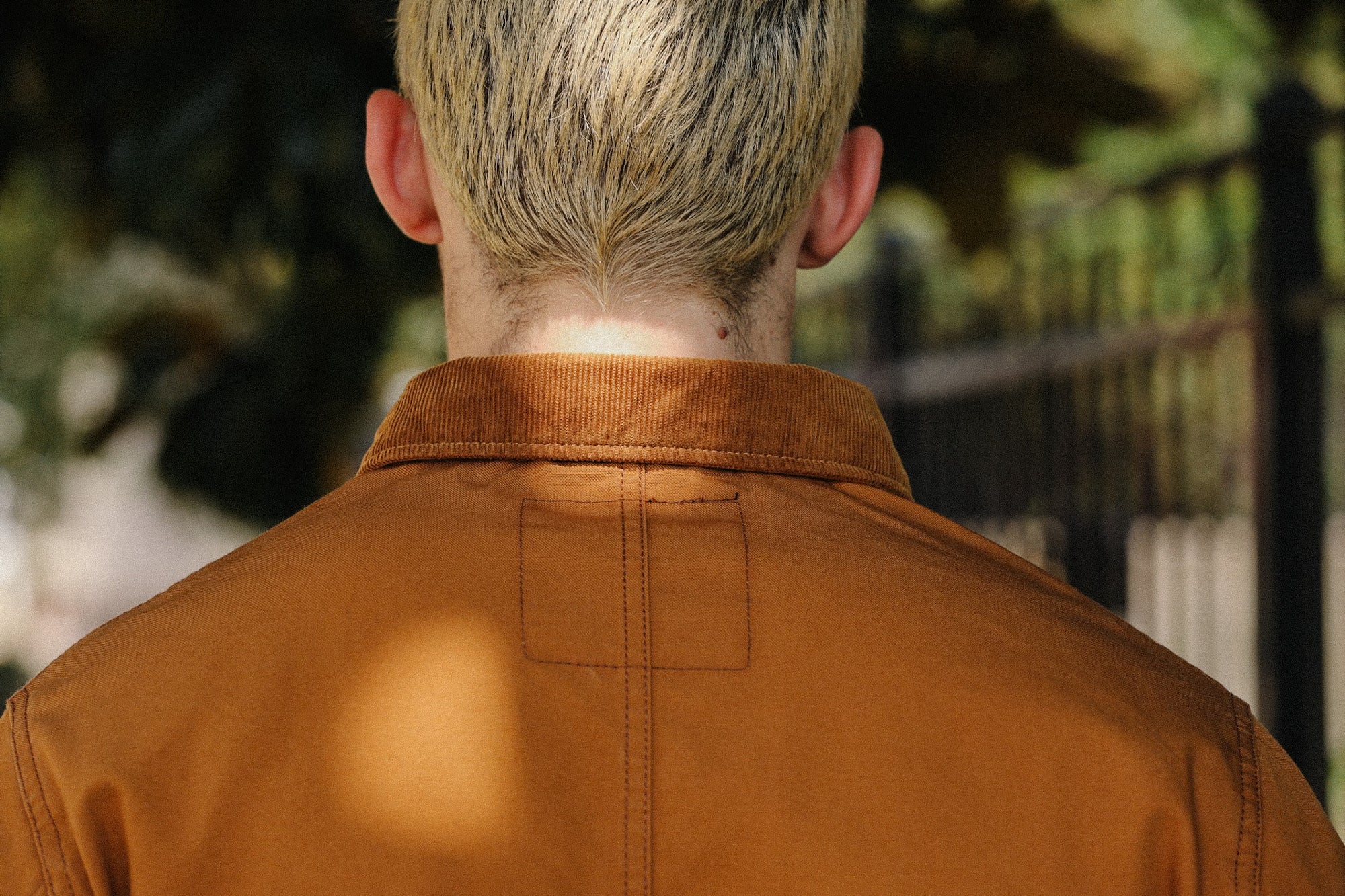 Rear view of person with short blonde hair wearing a brown corduroy collar jacket outdoors
