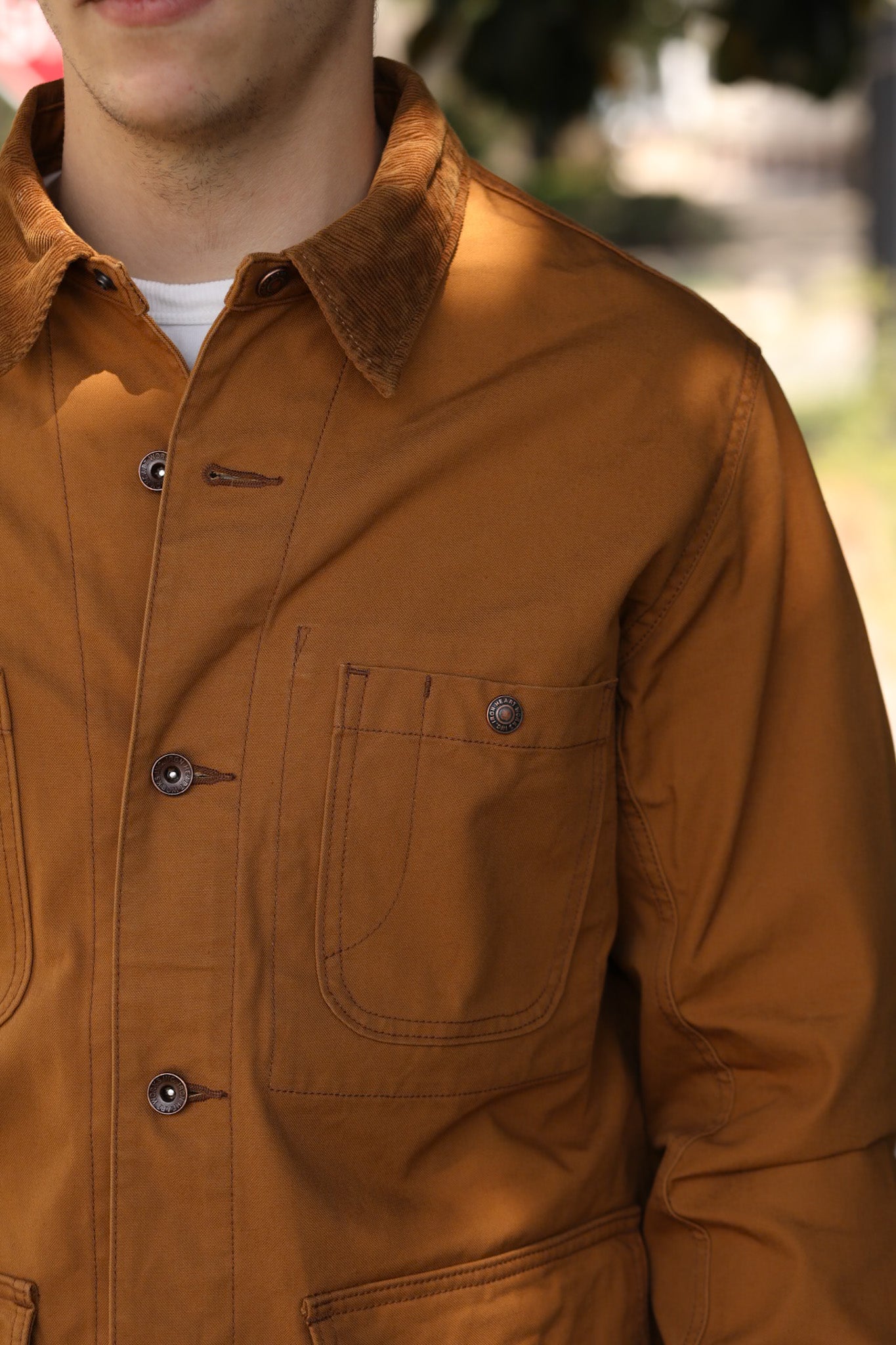 Close-up of a man wearing a brown workwear jacket with buttoned pockets and corduroy collar