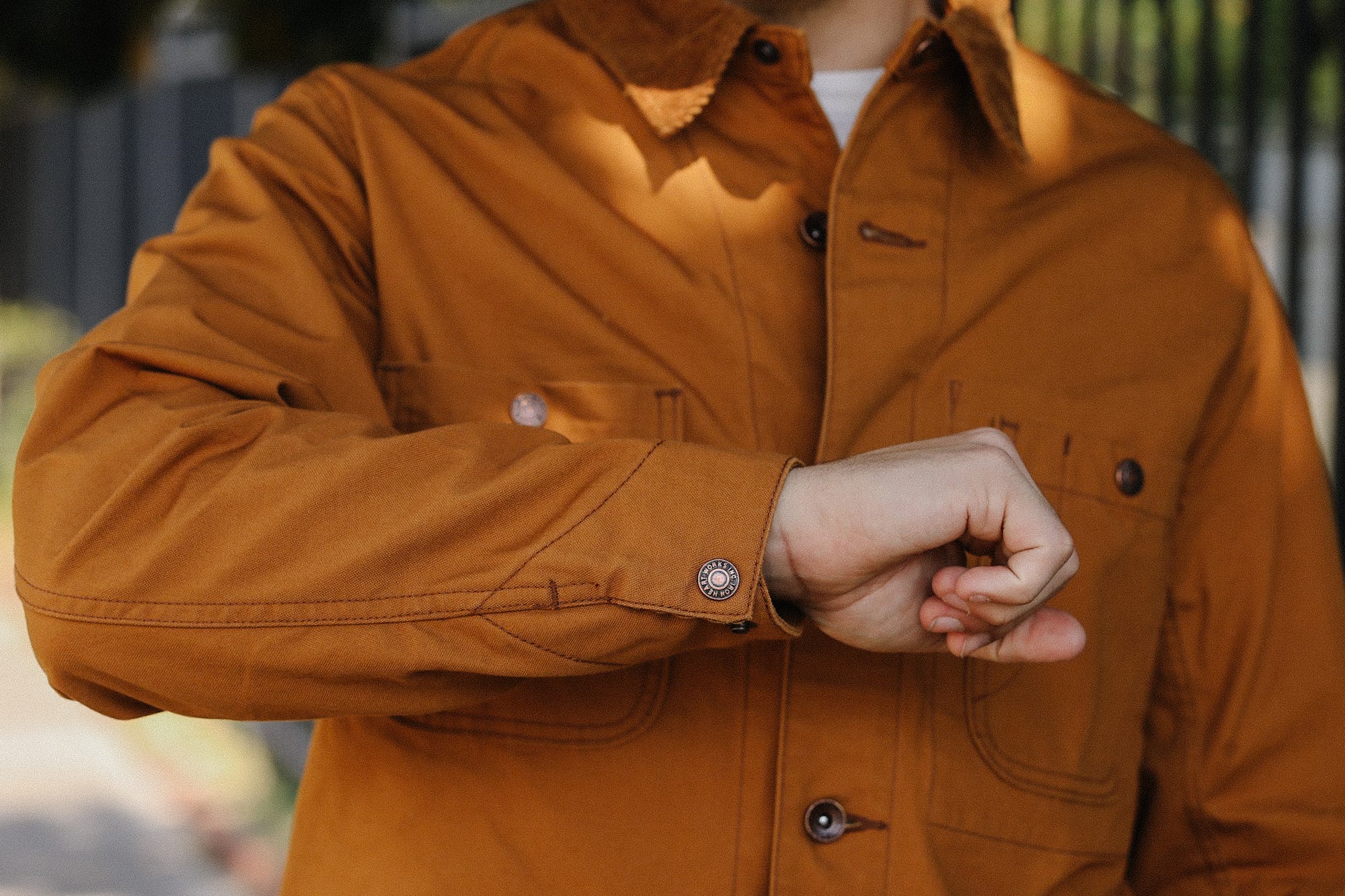 Close-up of person wearing brown work jacket with buttoned cuff outdoors