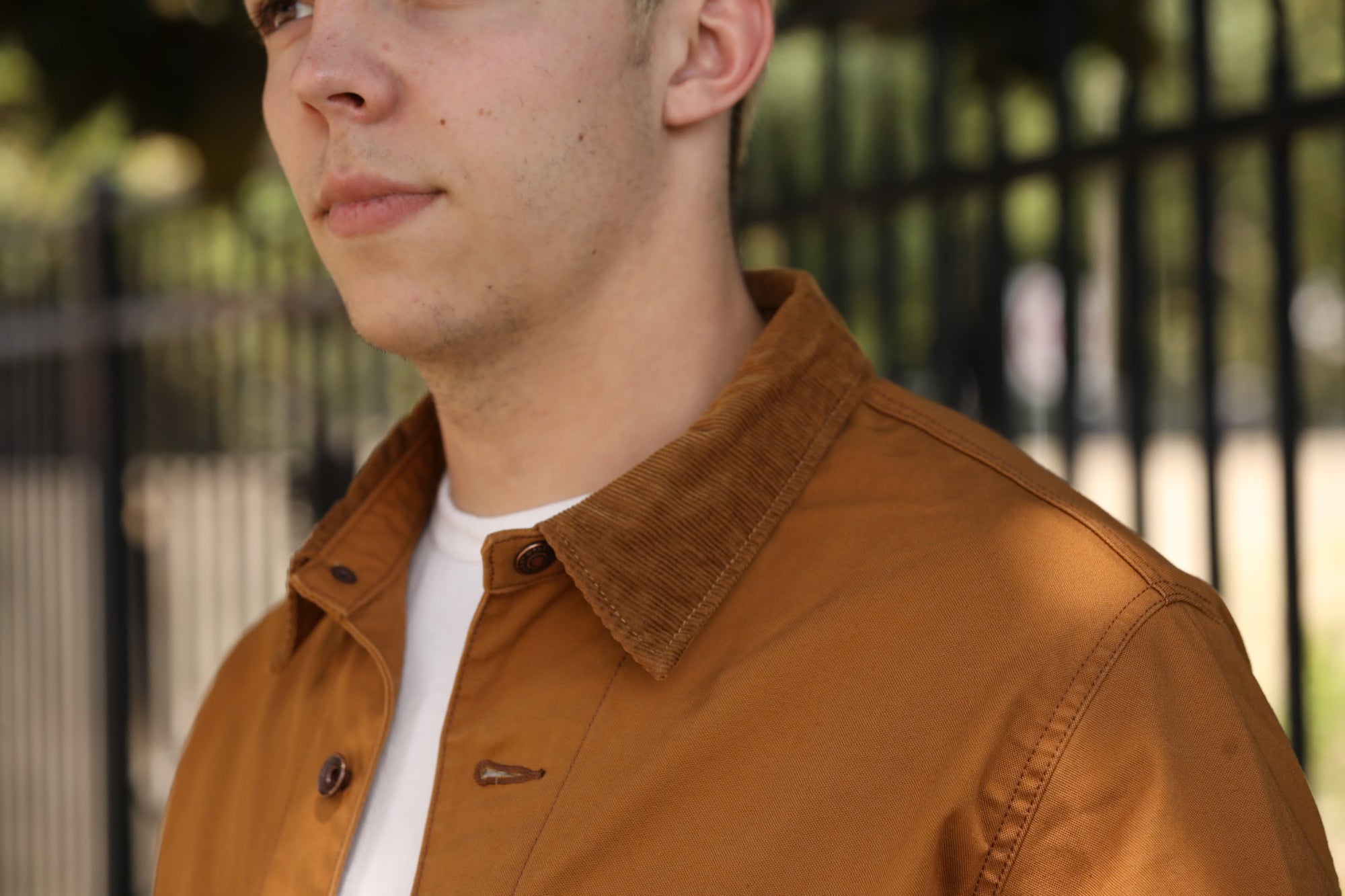 Close-up of a man wearing a brown canvas jacket with corduroy collar over white t-shirt outdoors