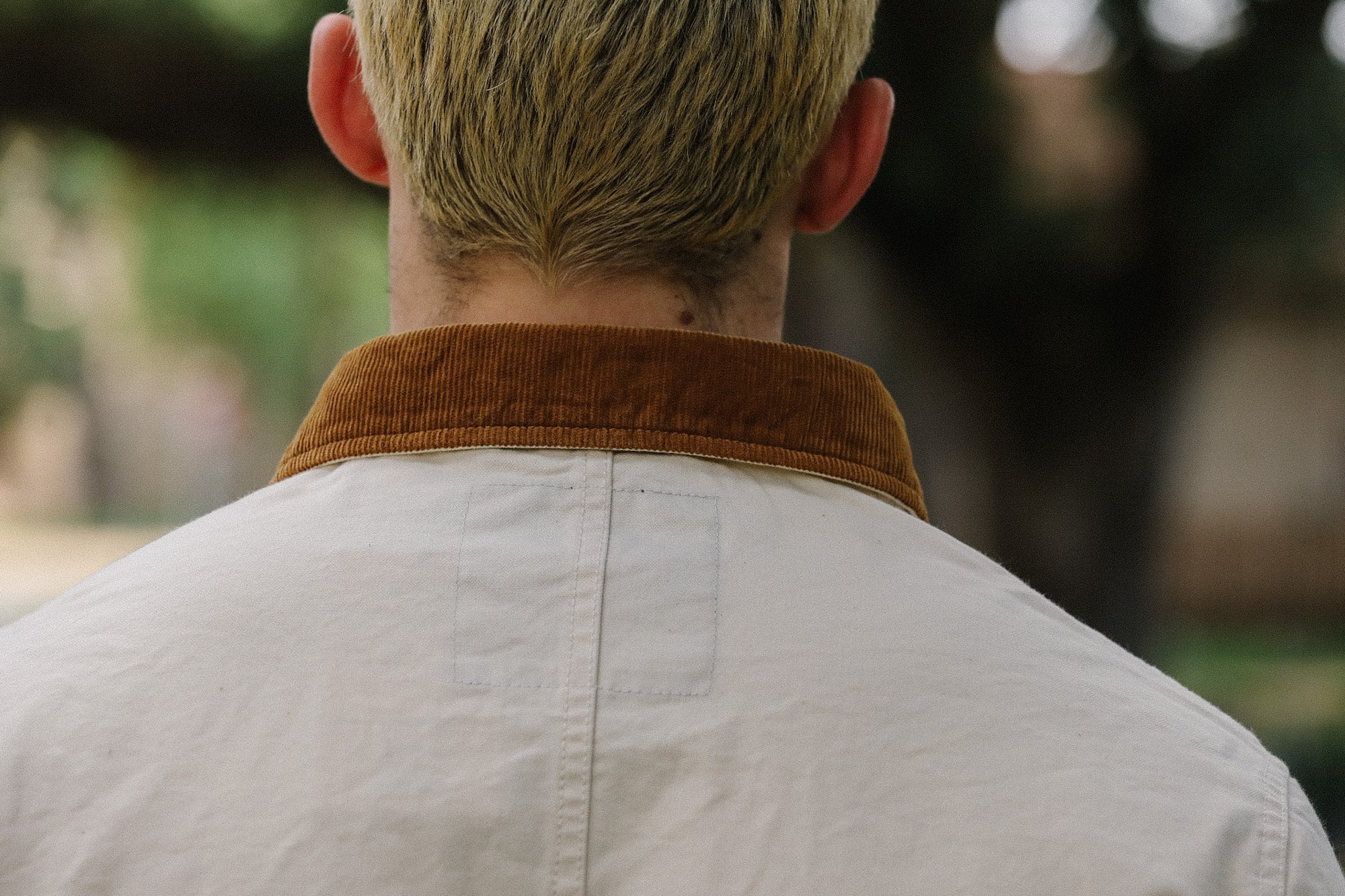 Back view of person wearing beige work jacket with brown corduroy collar in outdoor setting