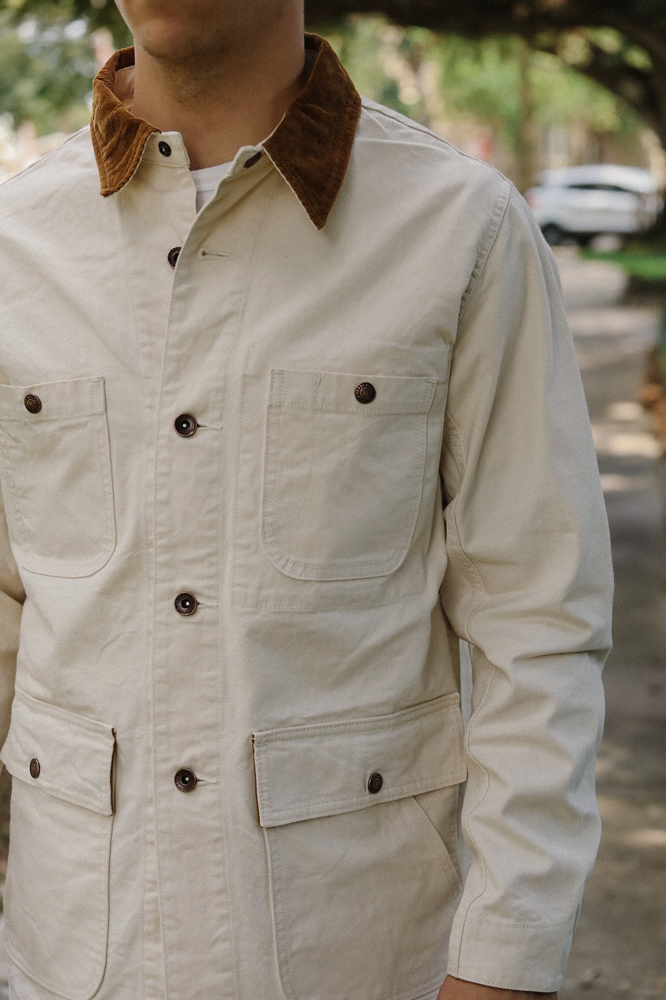 Close-up of a beige canvas jacket with brown corduroy collar and buttoned chest and flap pockets