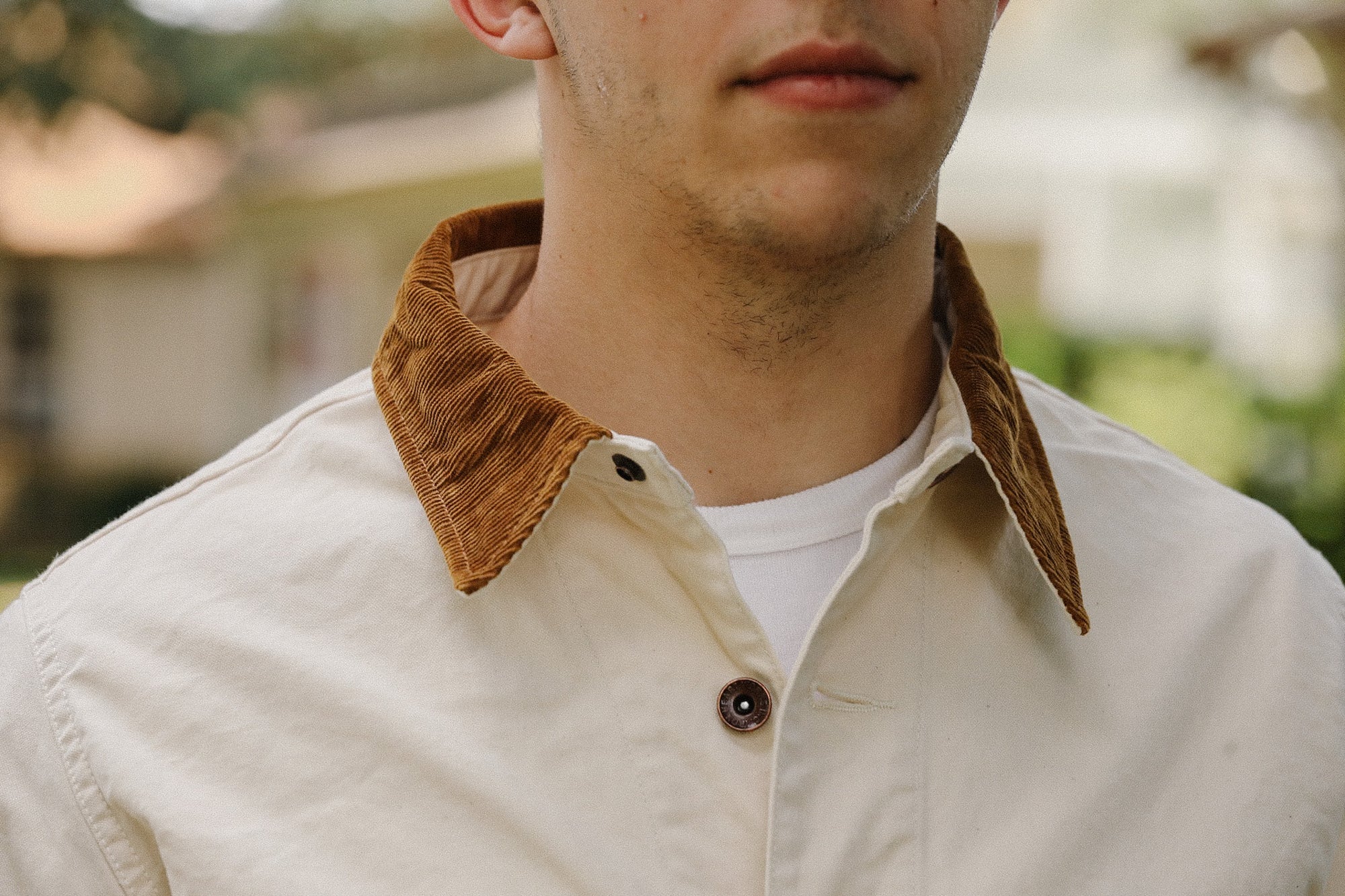 close-up of a man wearing a cream jacket with brown corduroy collar and white shirt underneath