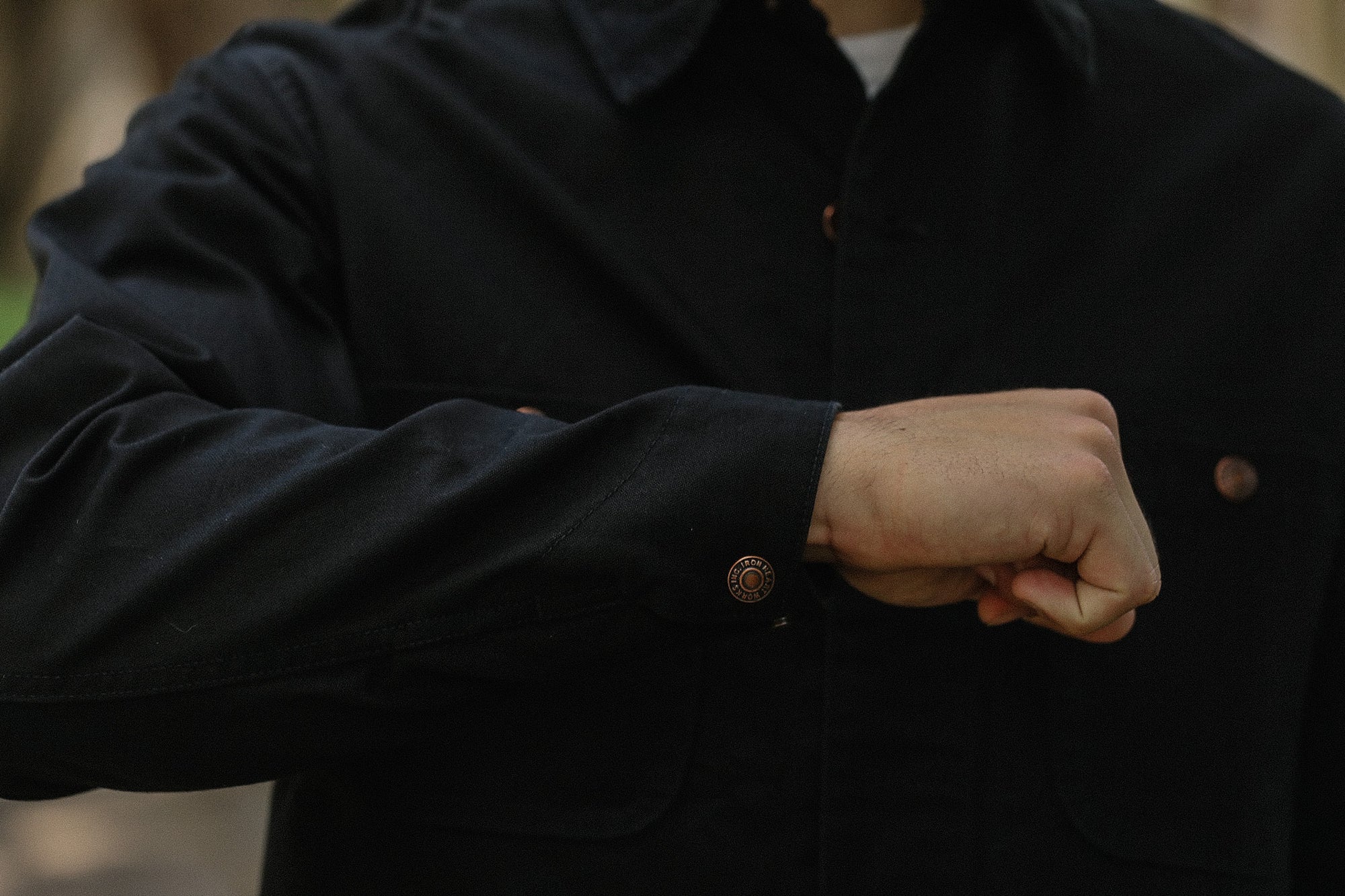 Close-up of a person wearing a black Iron Shop Provisions jacket with cuff button detail