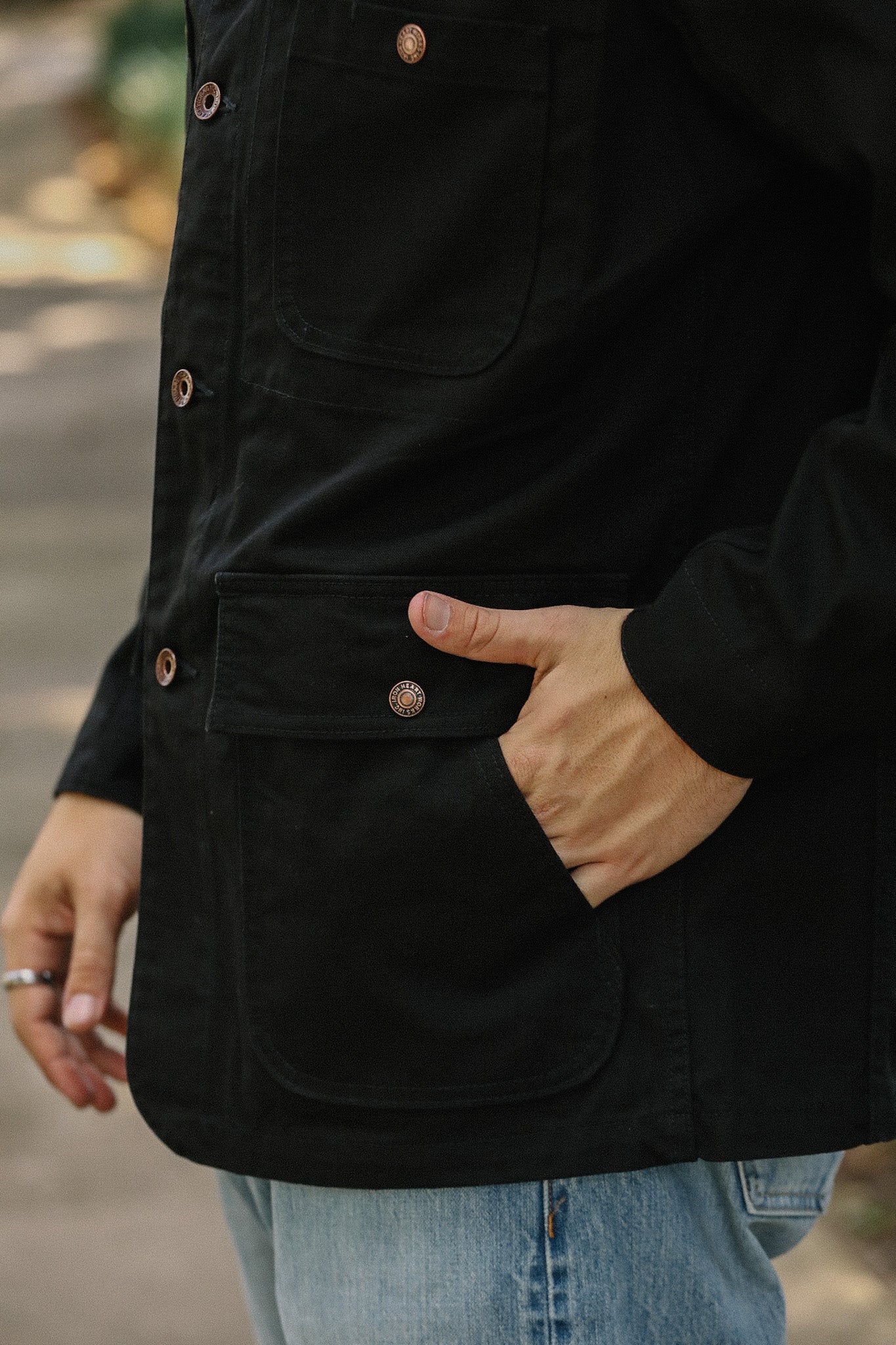 Close-up of a hand in the pocket of a black iron buttoned jacket with blue jeans outdoors