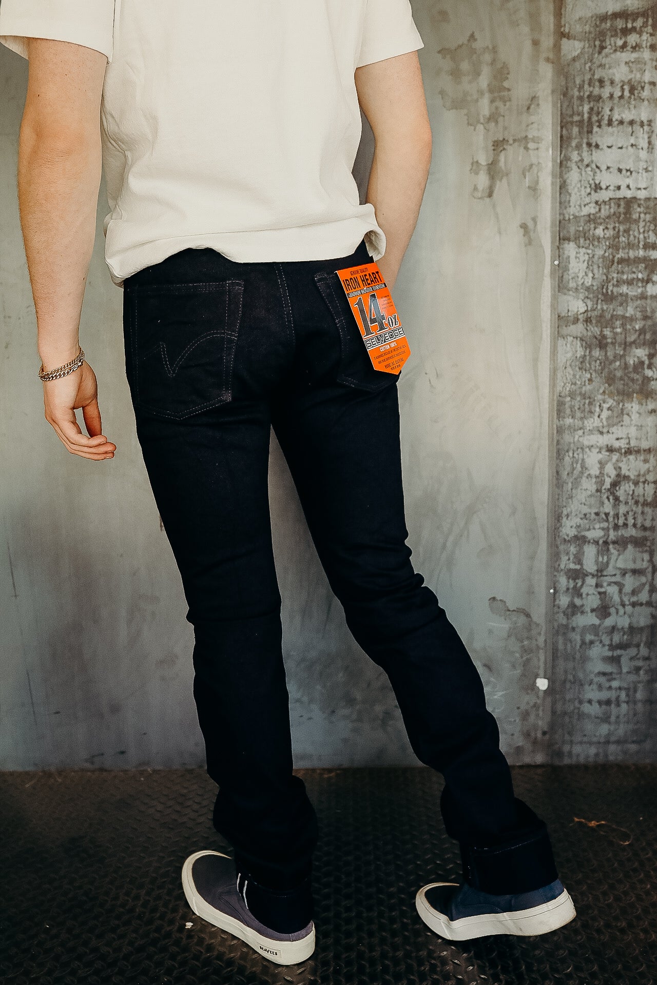 Person wearing slim fit black Iron Heart 14 oz selvage denim jeans with rolled cuffs and sneakers