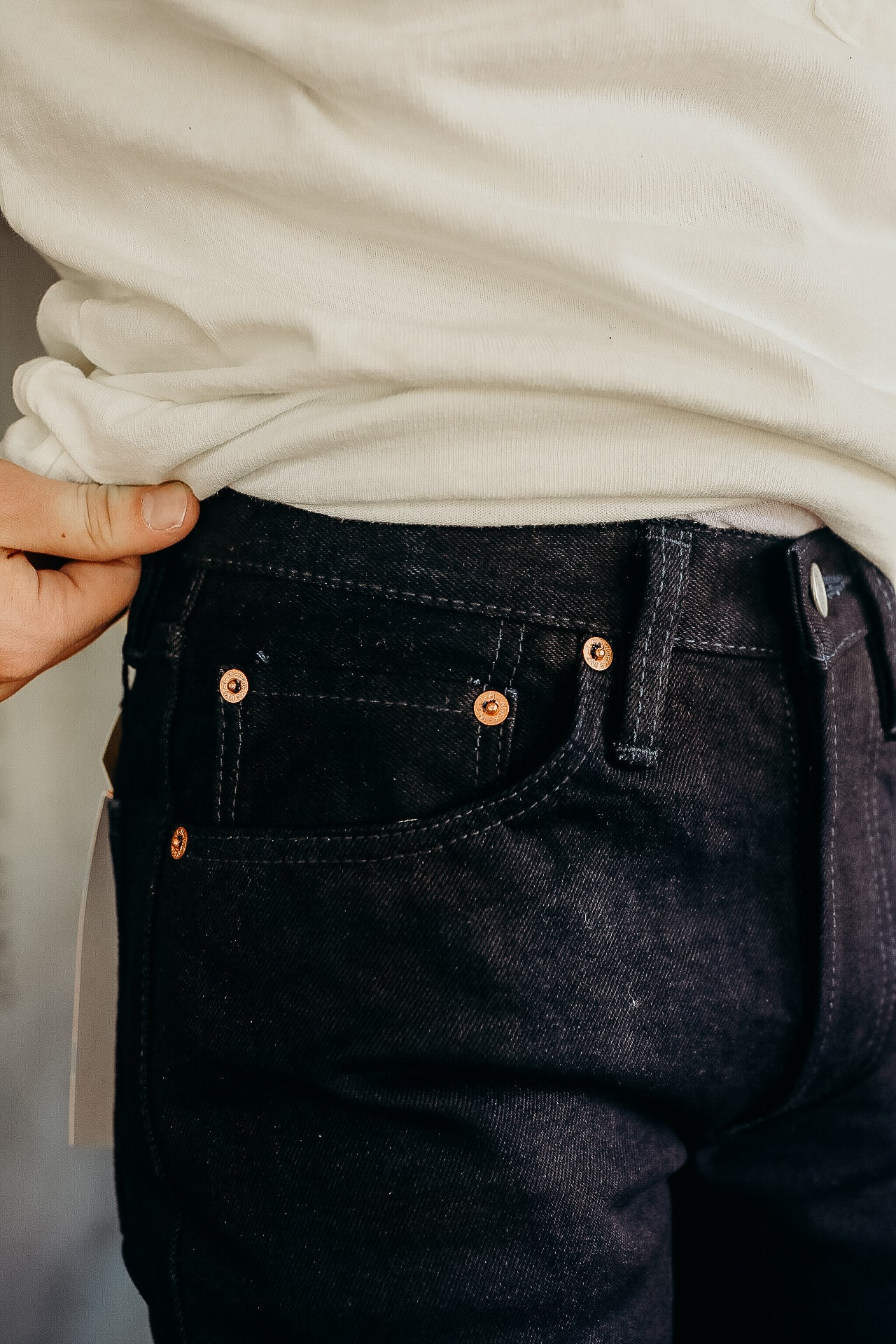 Close-up of a person wearing black denim jeans with copper rivets and a white shirt tucked in