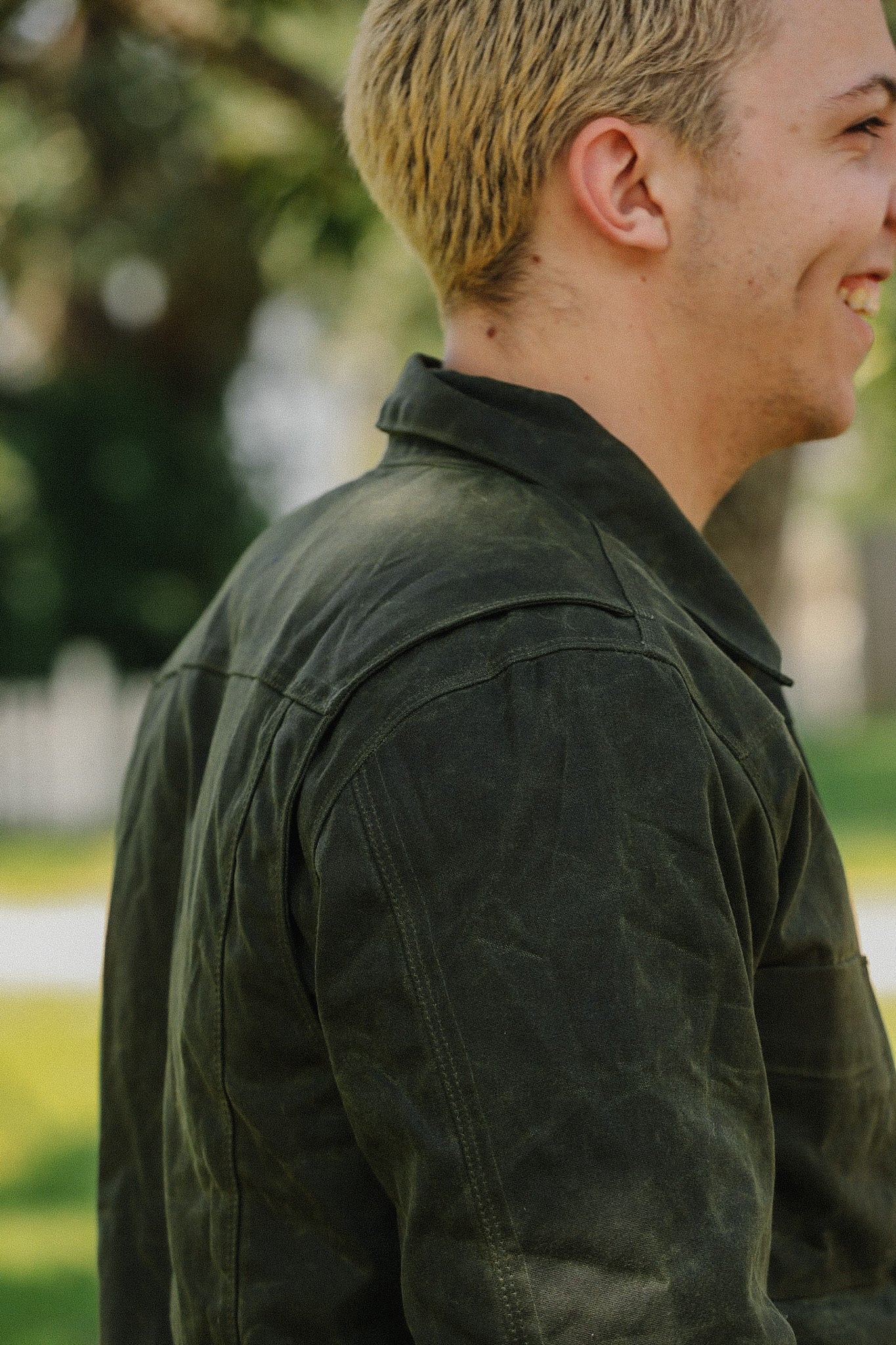 Close-up side view of a smiling young man wearing a dark green rugged jacket outdoors