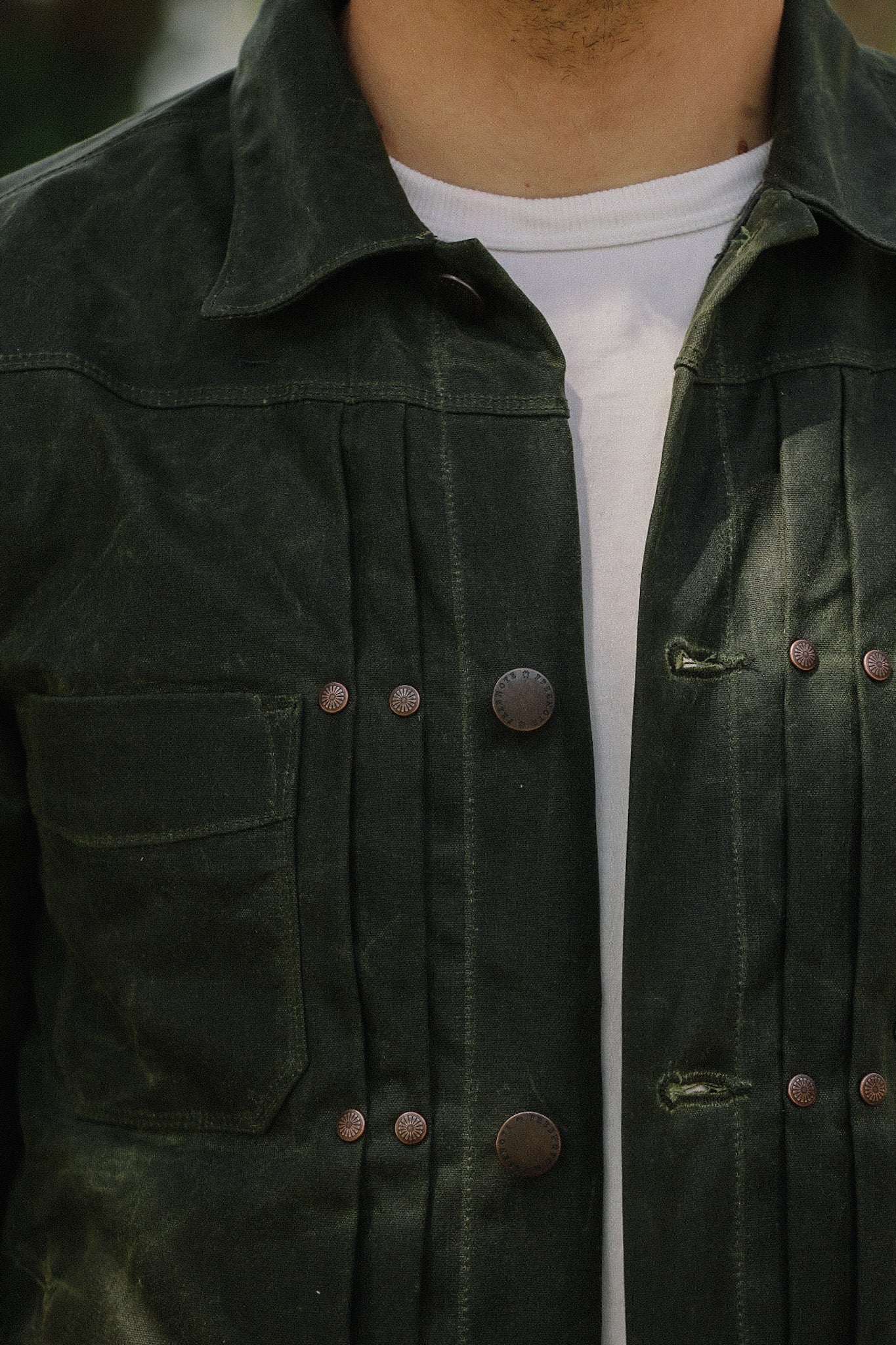 Close-up of dark green rugged jacket with metal buttons over a white shirt, showcasing durable workwear style