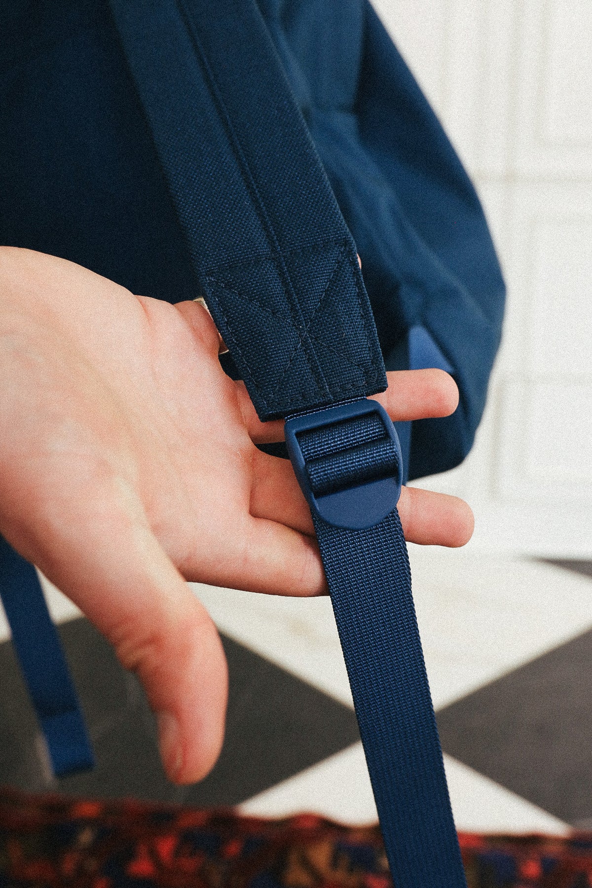 Close-up of a person's hand adjusting the strap and plastic buckle of a navy blue backpack.