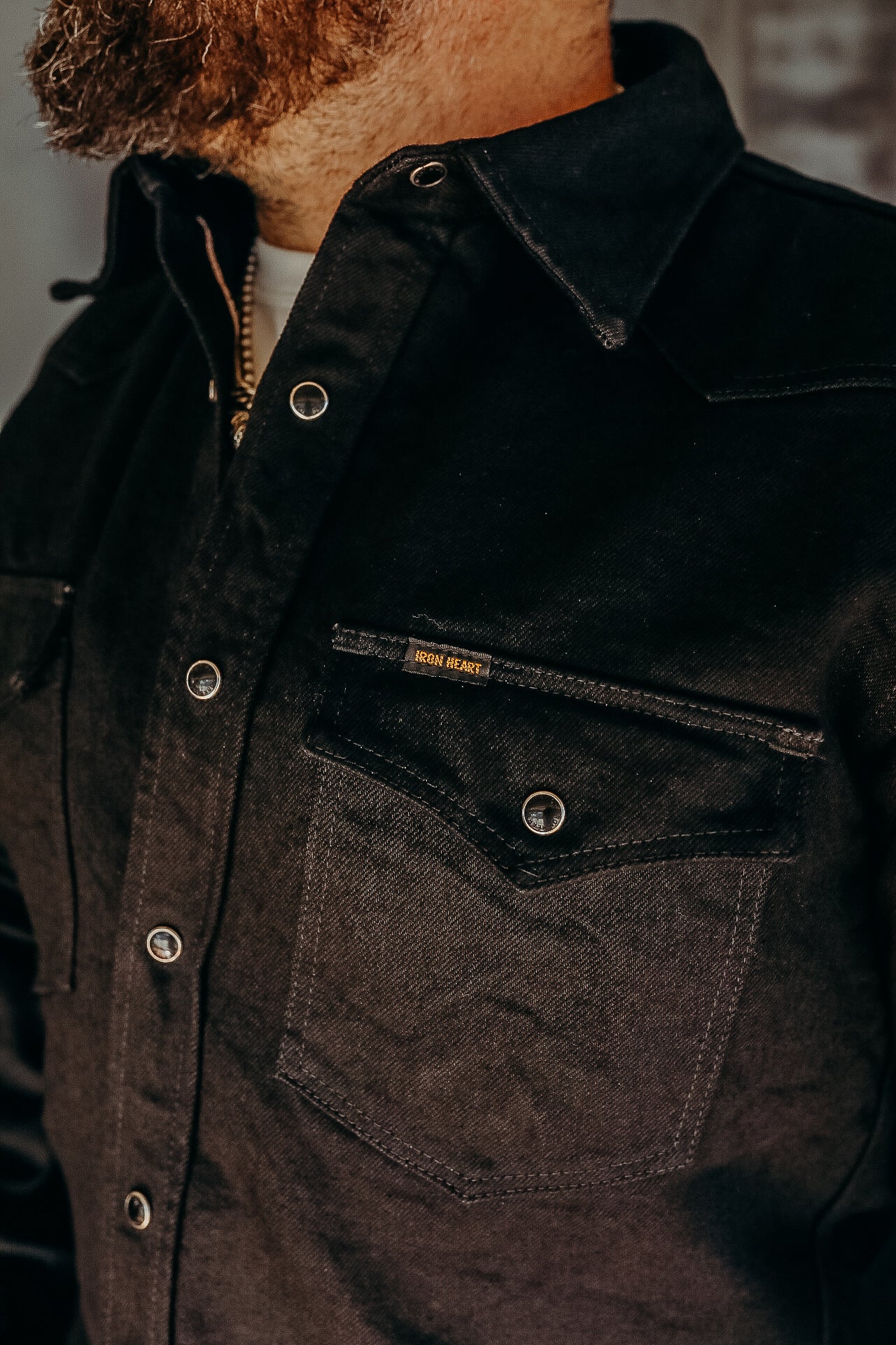 Close-up of a man wearing a black Iron Heart work shirt with snap buttons and chest pocket detail