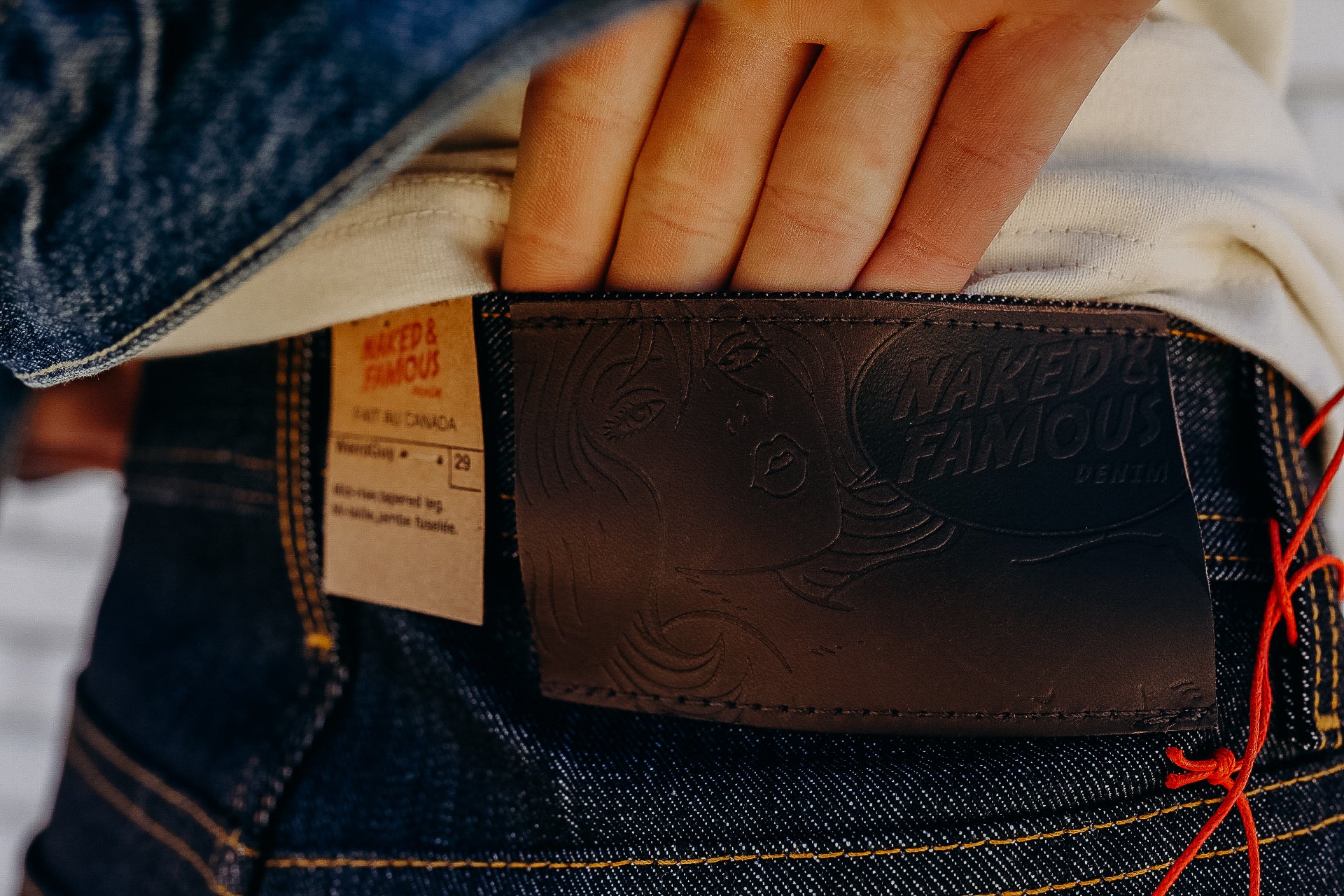 Close-up of hand showing Naked &amp; Famous denim leather patch and fabric label on dark blue jeans
