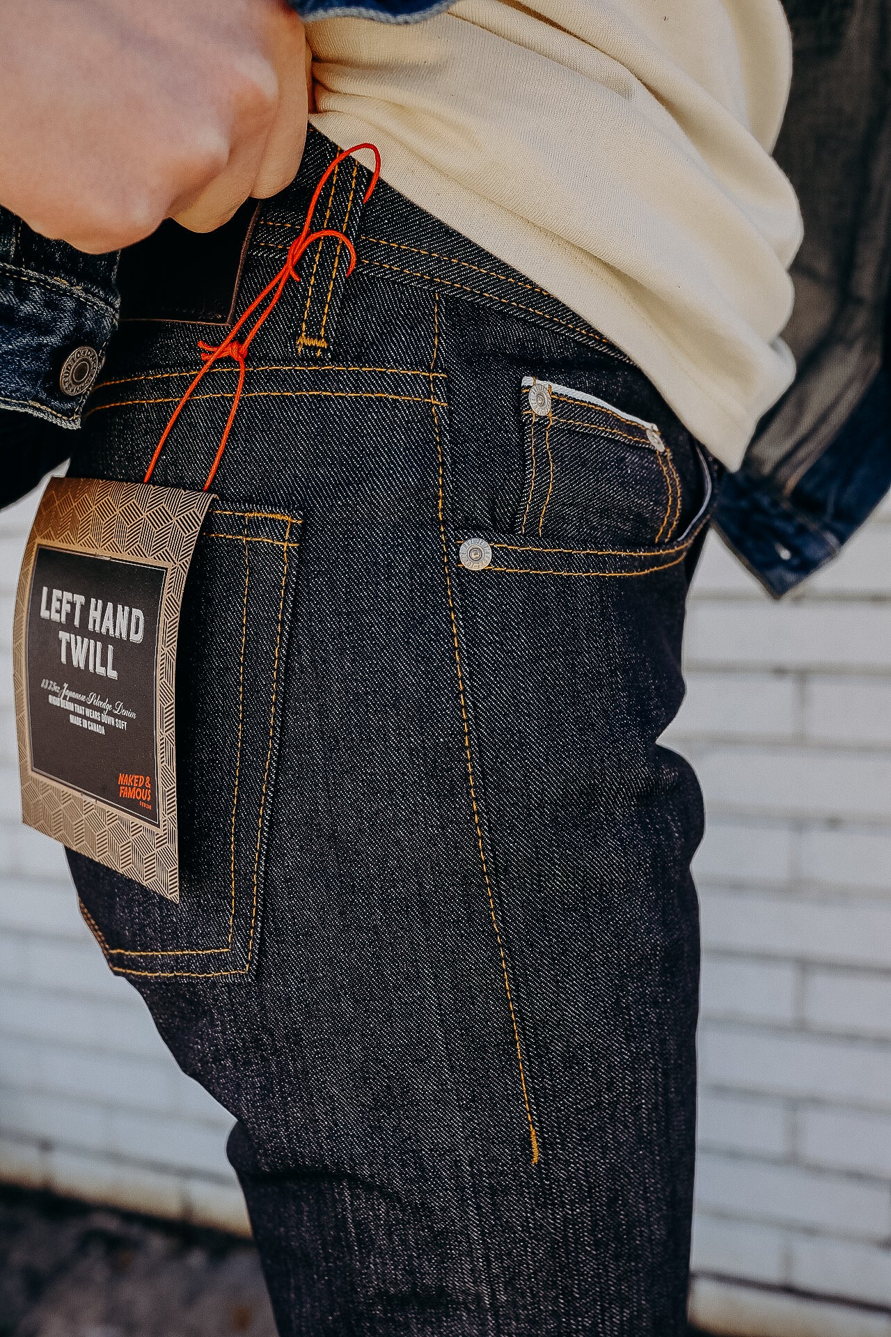 Close-up of person wearing dark raw denim jeans with orange stitching and a Left Hand Twill tag