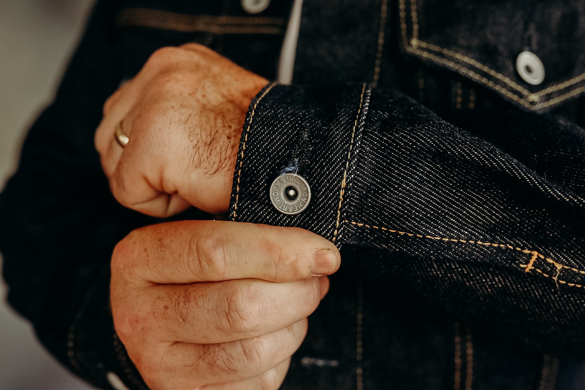 Close-up of a person's hand fastening a dark denim jacket cuff with metal button detail
