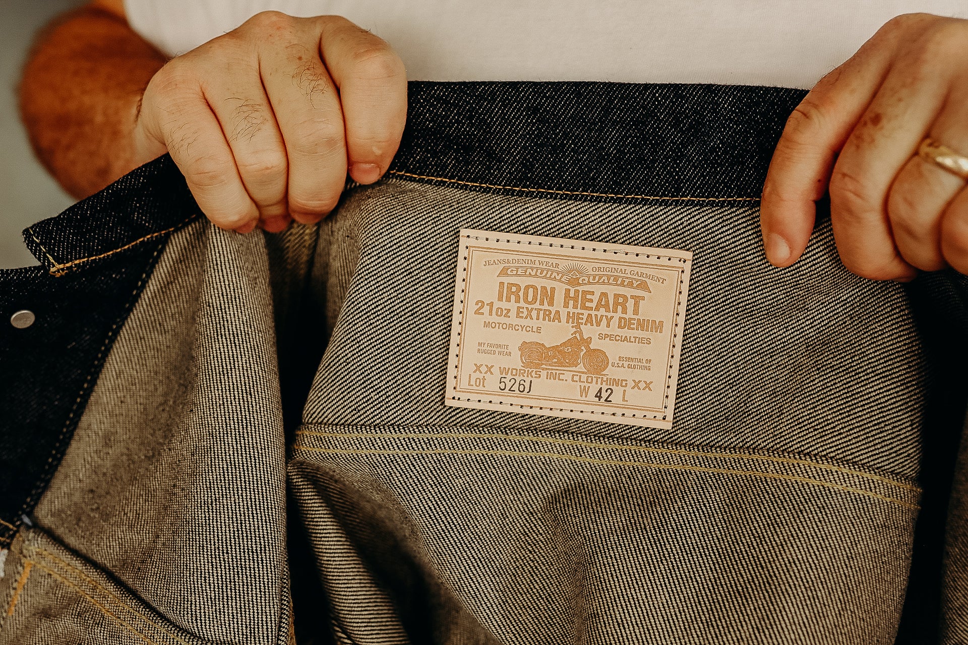 Hands holding open denim jeans showing Iron Heart 21oz extra heavy denim label inside waistband