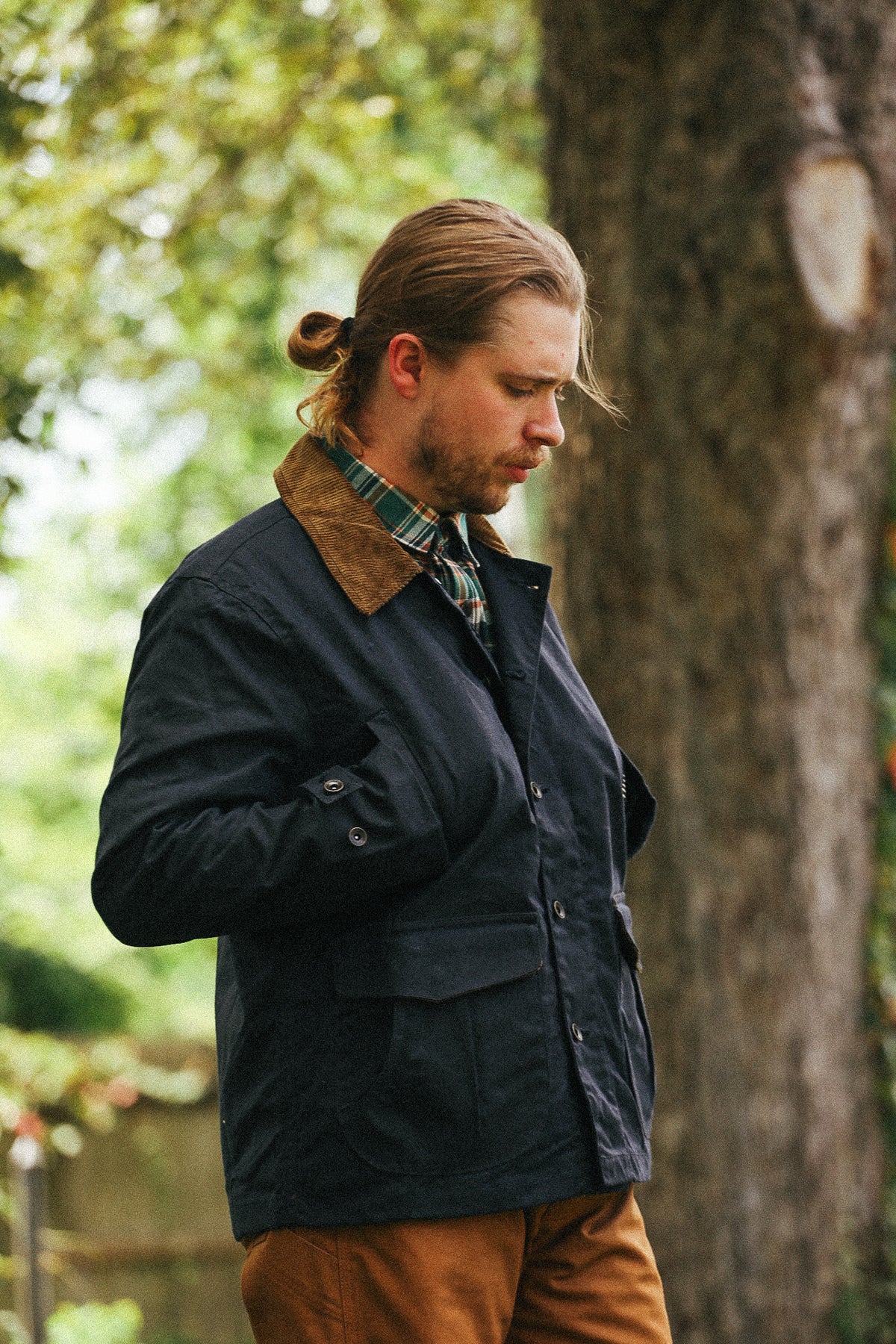 man standing with black jacket and green shirt against a green natural background