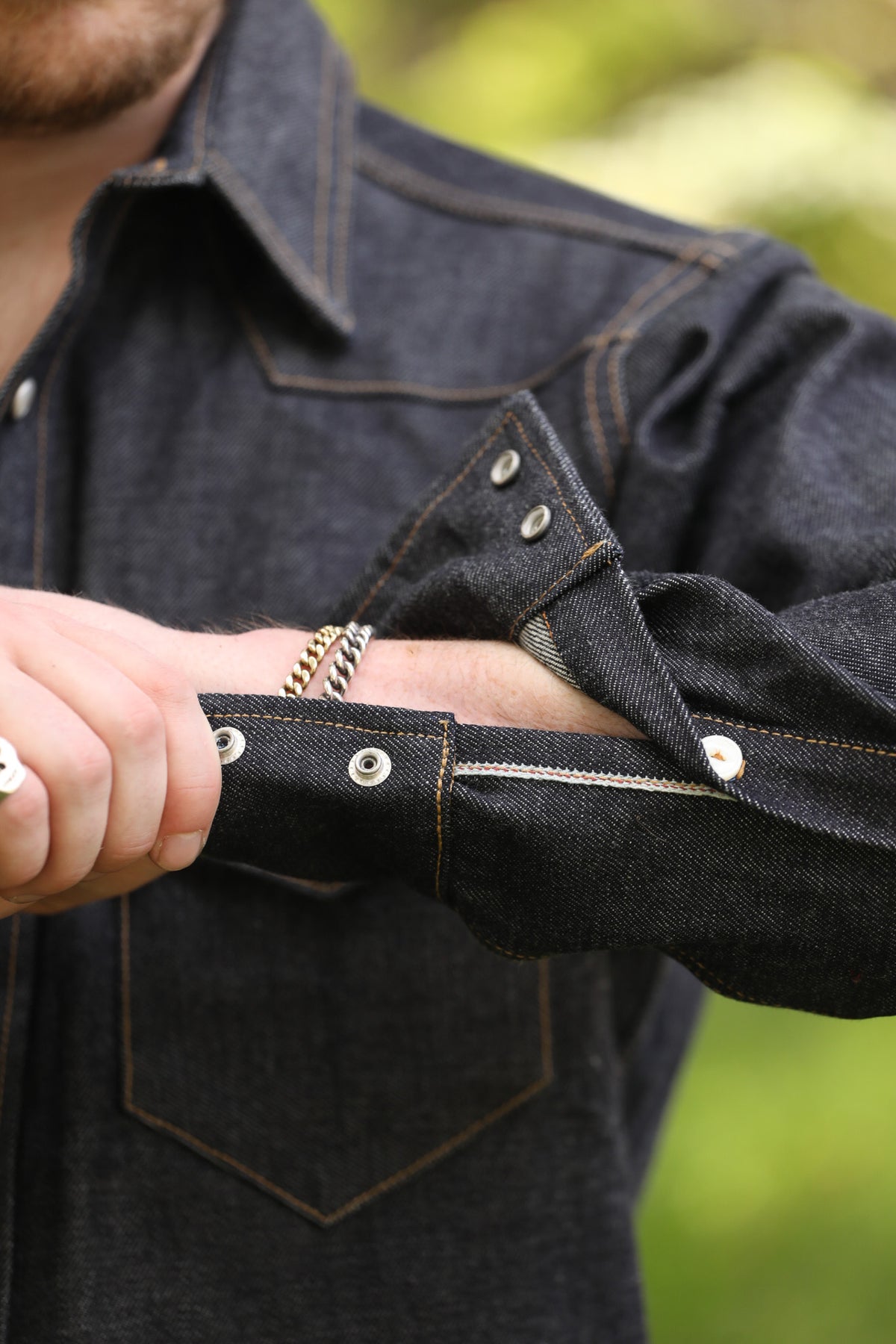 man with denim shirt showing cuff detail against a green natural background