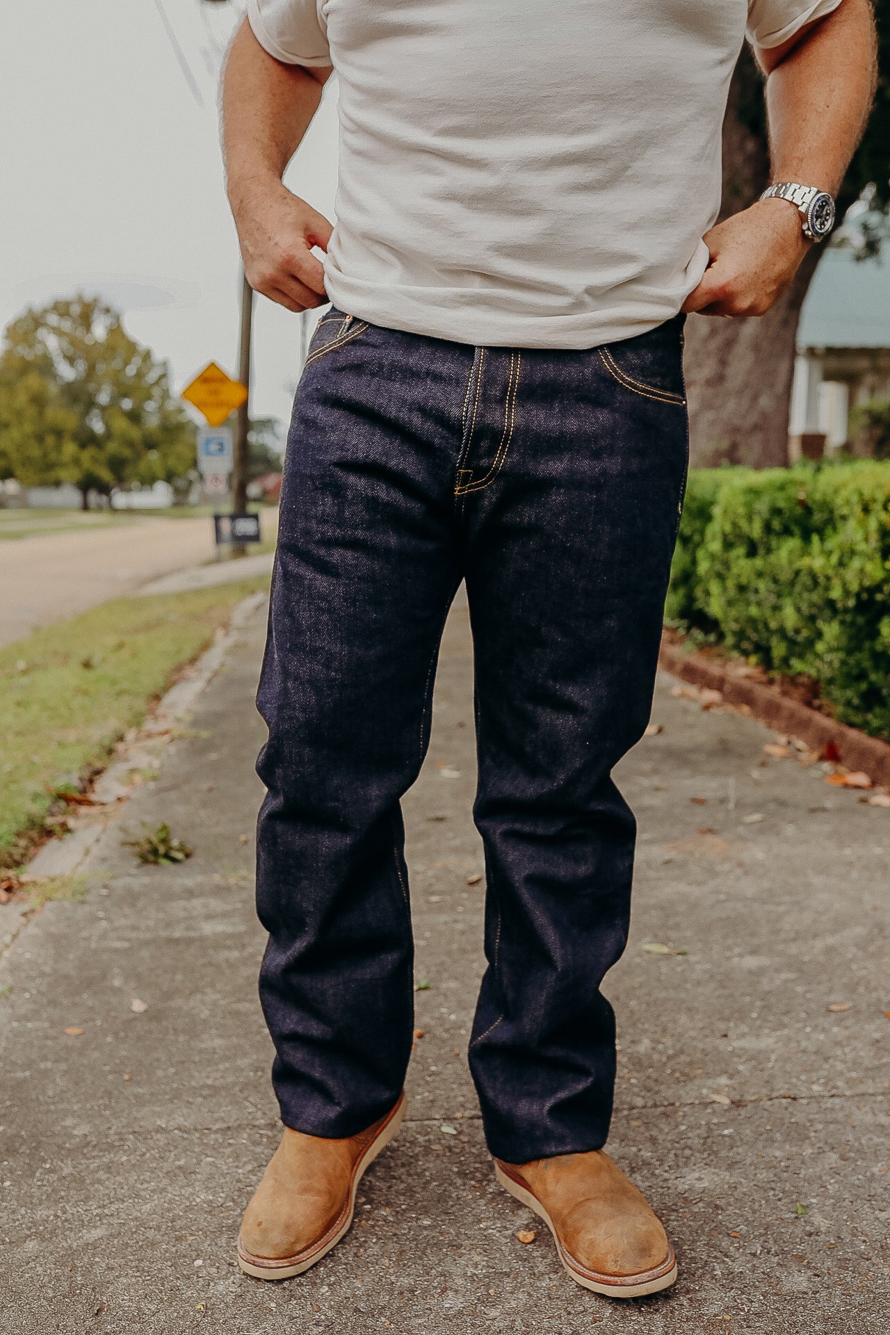 Man wearing raw denim jeans and brown boots standing on a sidewalk outdoors