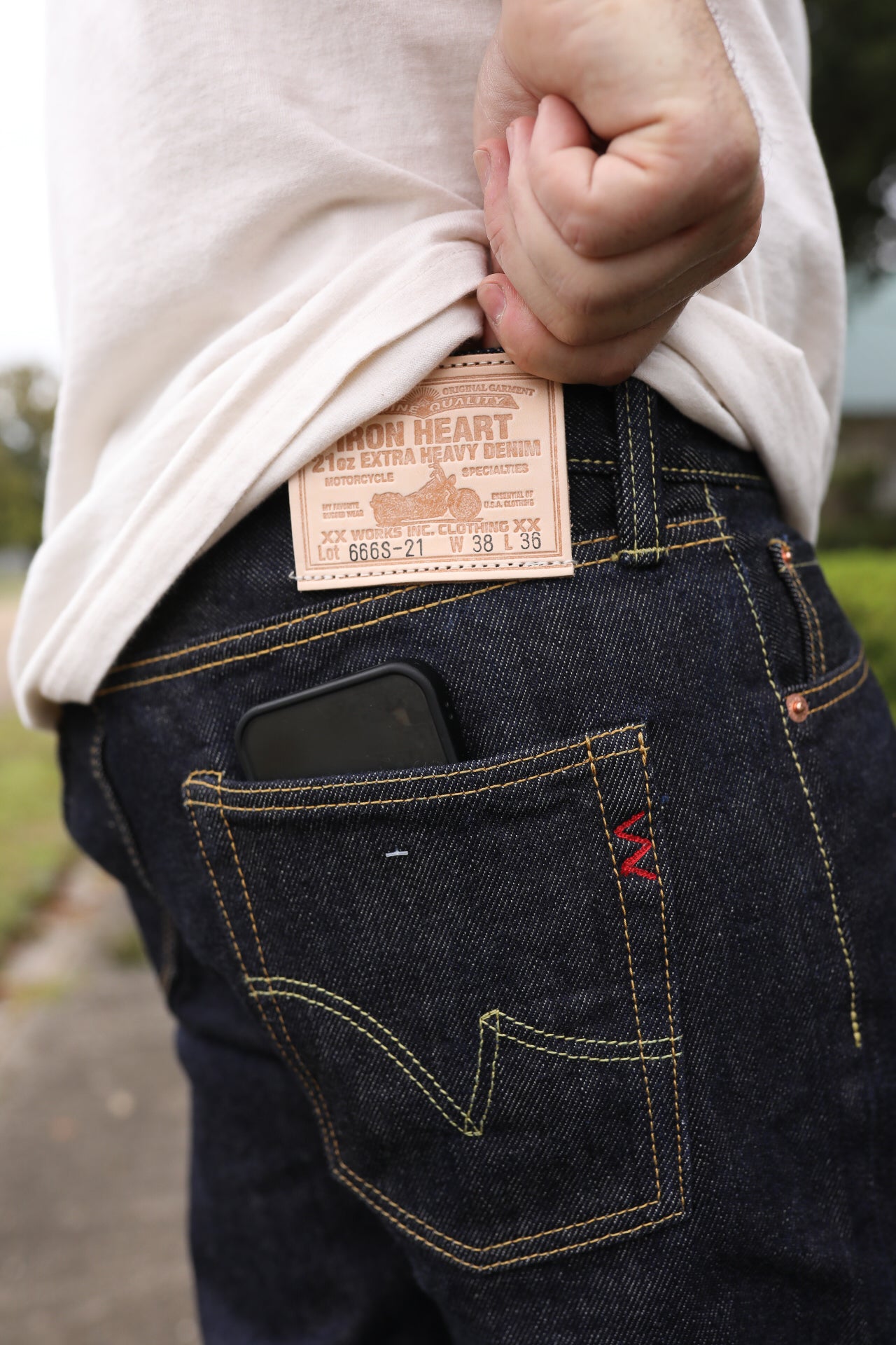 Close-up of person wearing Iron Heart 21oz extra heavy denim jeans with leather logo patch and phone in back pocket