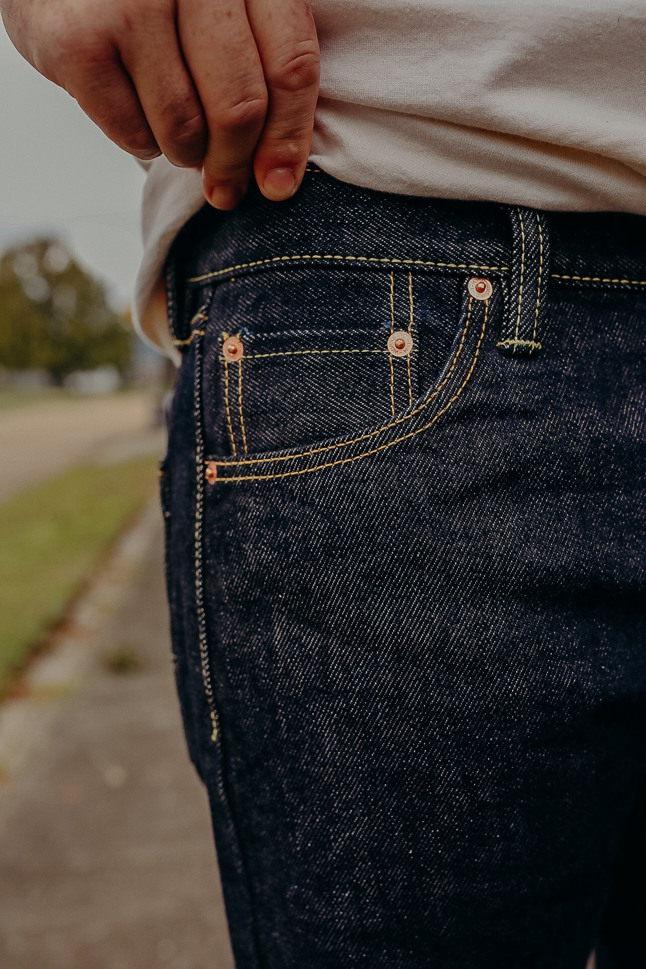 Close-up of hand near front pocket of dark blue denim jeans with yellow stitching outdoors