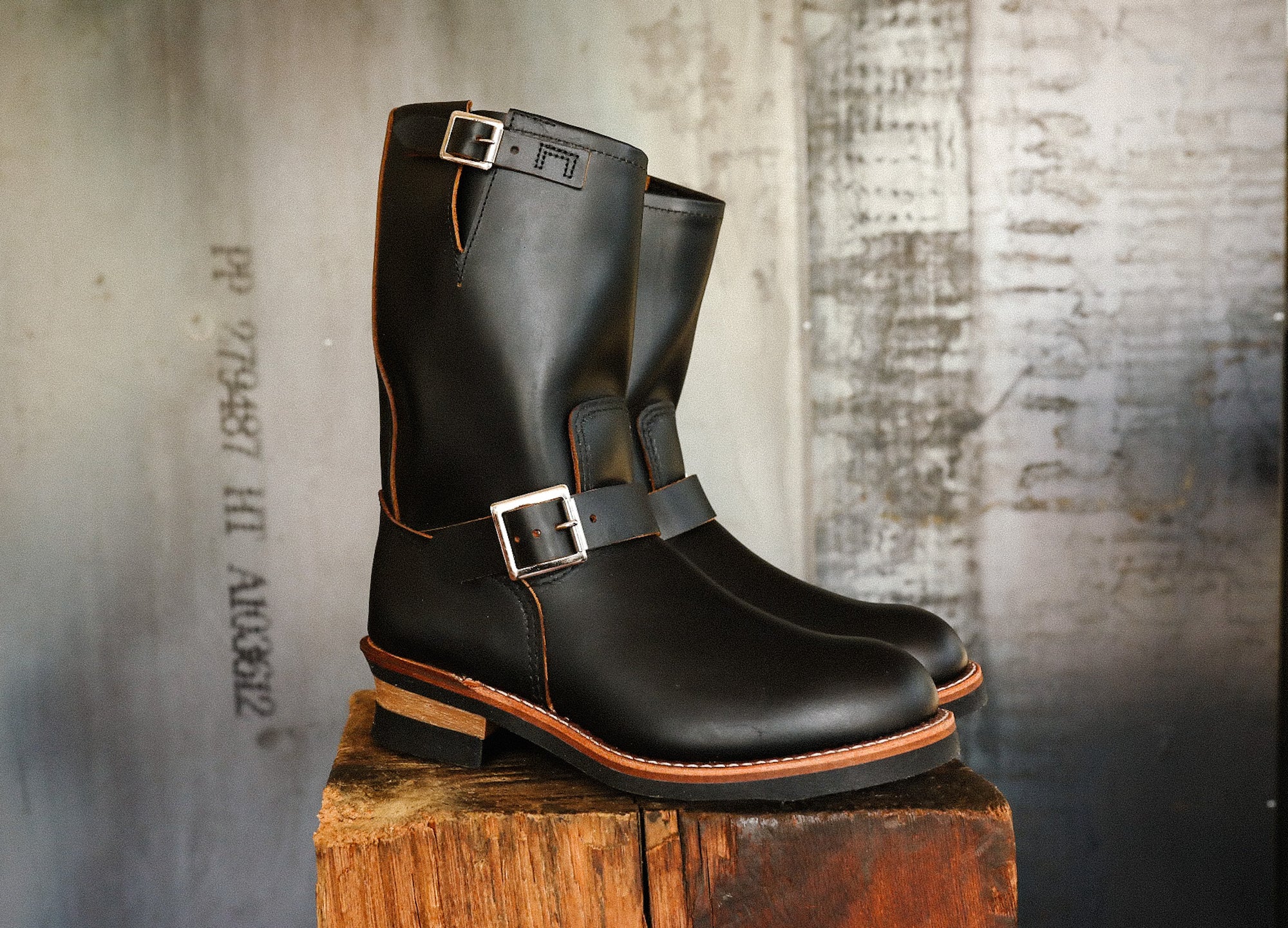 Pair of black leather engineer boots with silver buckles on rustic wooden block