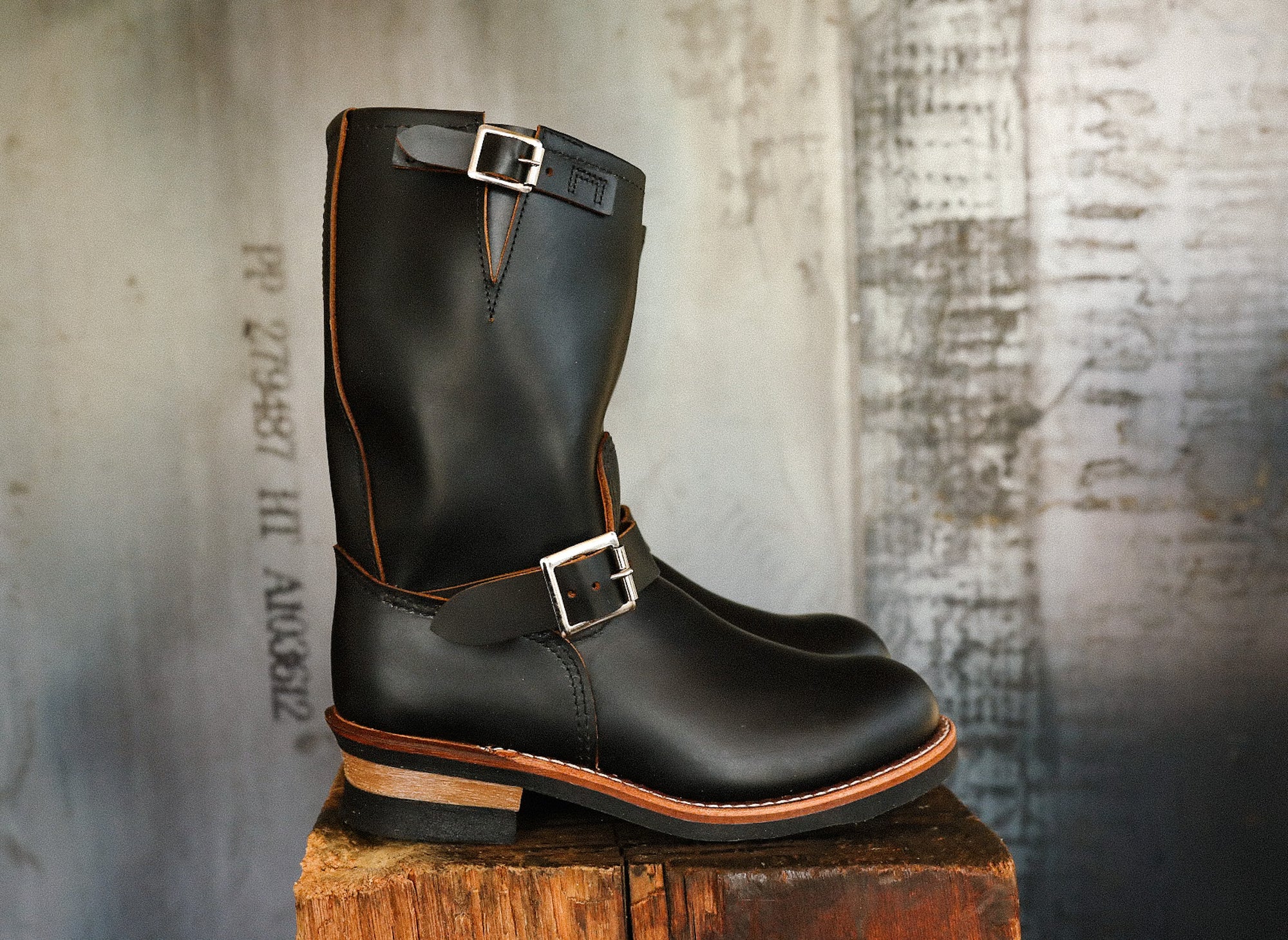 Black leather engineer boots with silver buckles on wooden block against rustic textured background