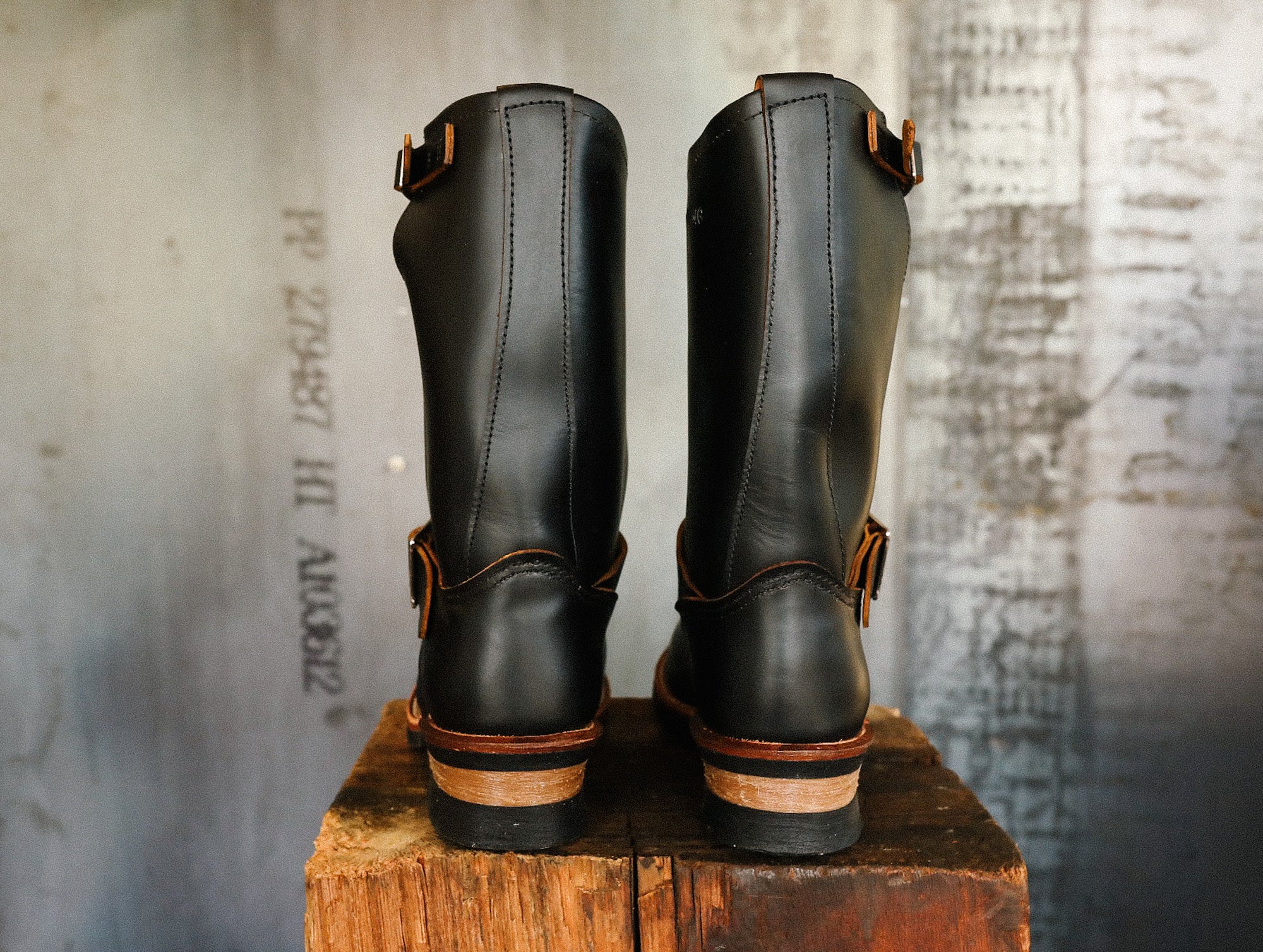 Back view of black leather work boots with leather straps on rustic wooden block