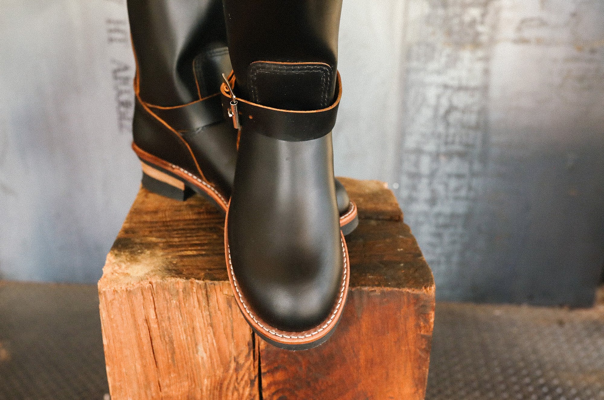 Black leather engineer boots with brown stitching displayed on a rustic wooden block at Iron Shop Provisions