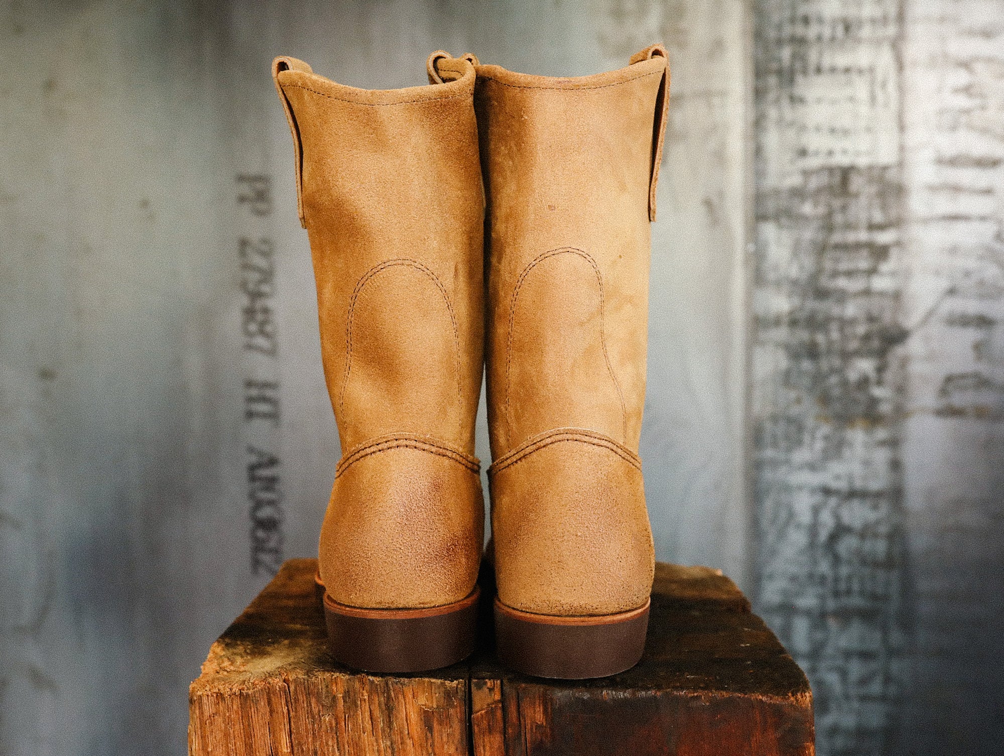 Pair of tan leather work boots on rustic wooden block with industrial metal background