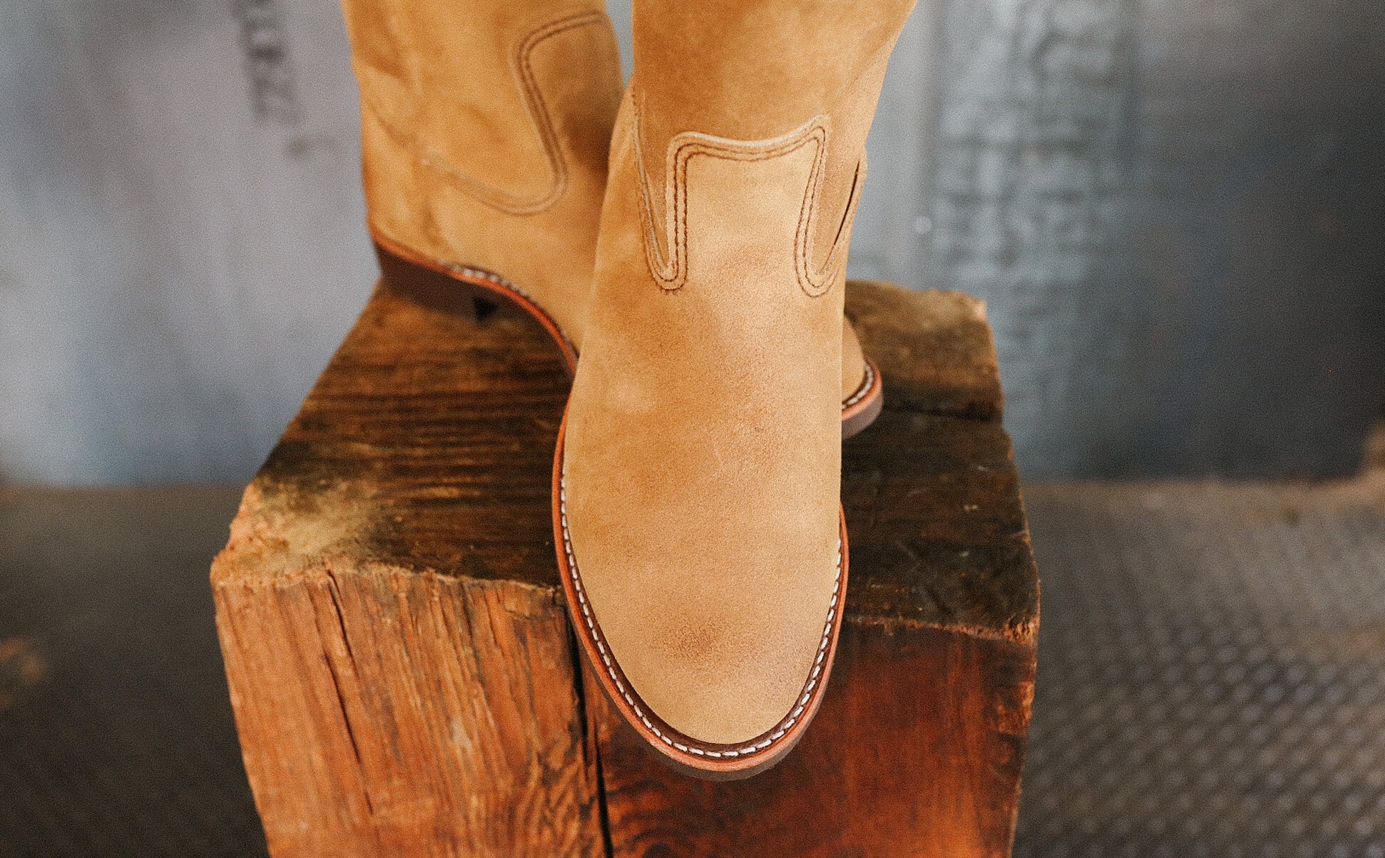 Close-up of tan suede cowboy boots on a rustic wooden block in industrial setting