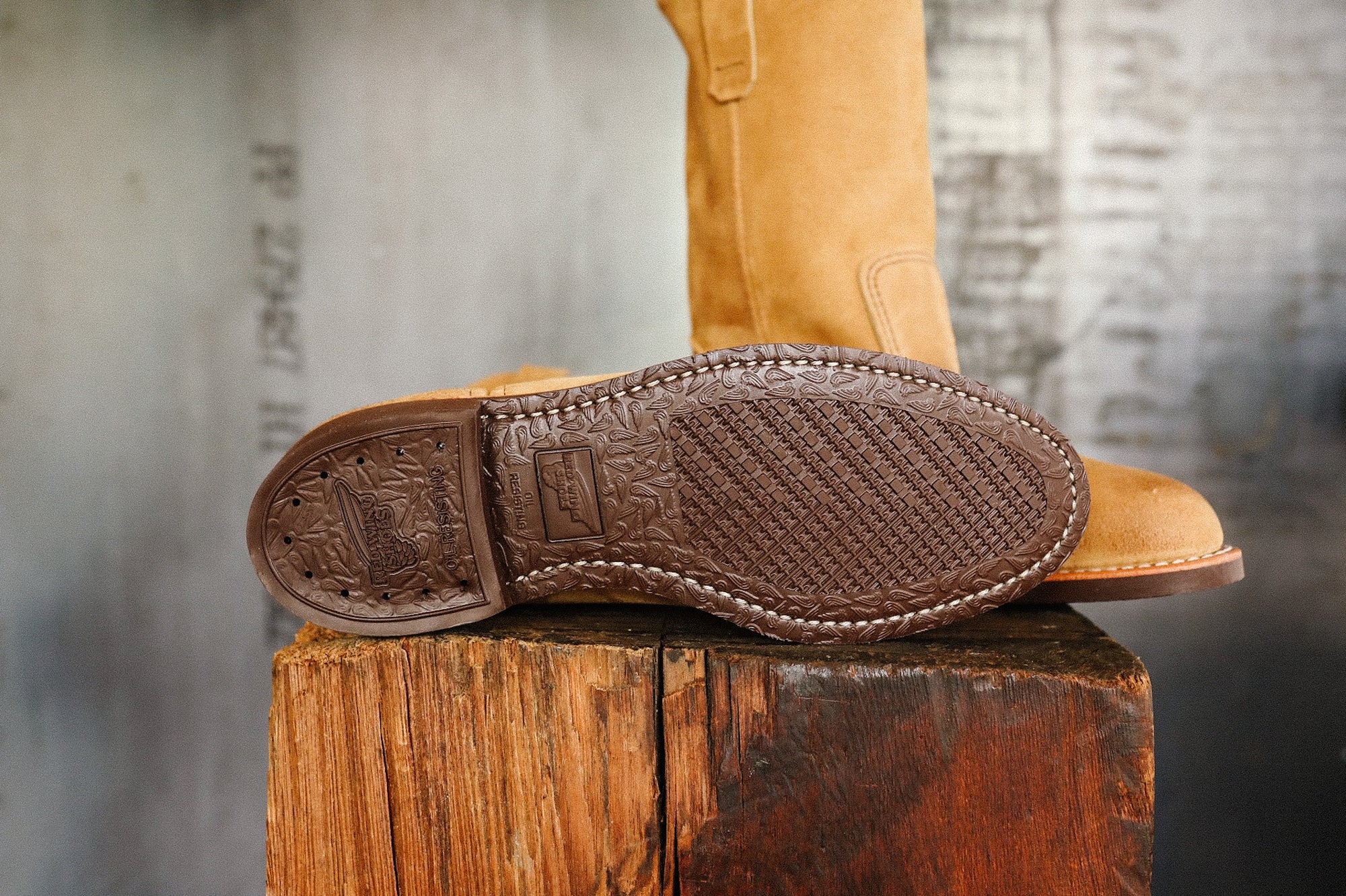 Close-up of brown sole and tan leather boot on rustic wooden block, rugged work footwear