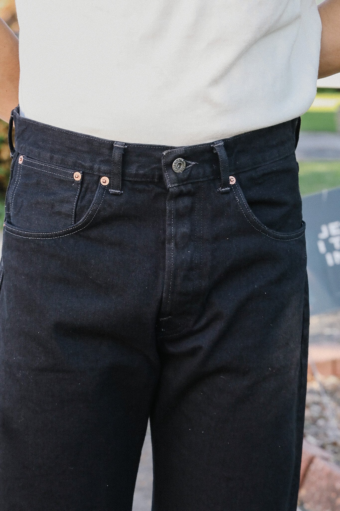Close-up of person wearing black denim jeans with copper rivets and button fly from Iron Shop Provisions