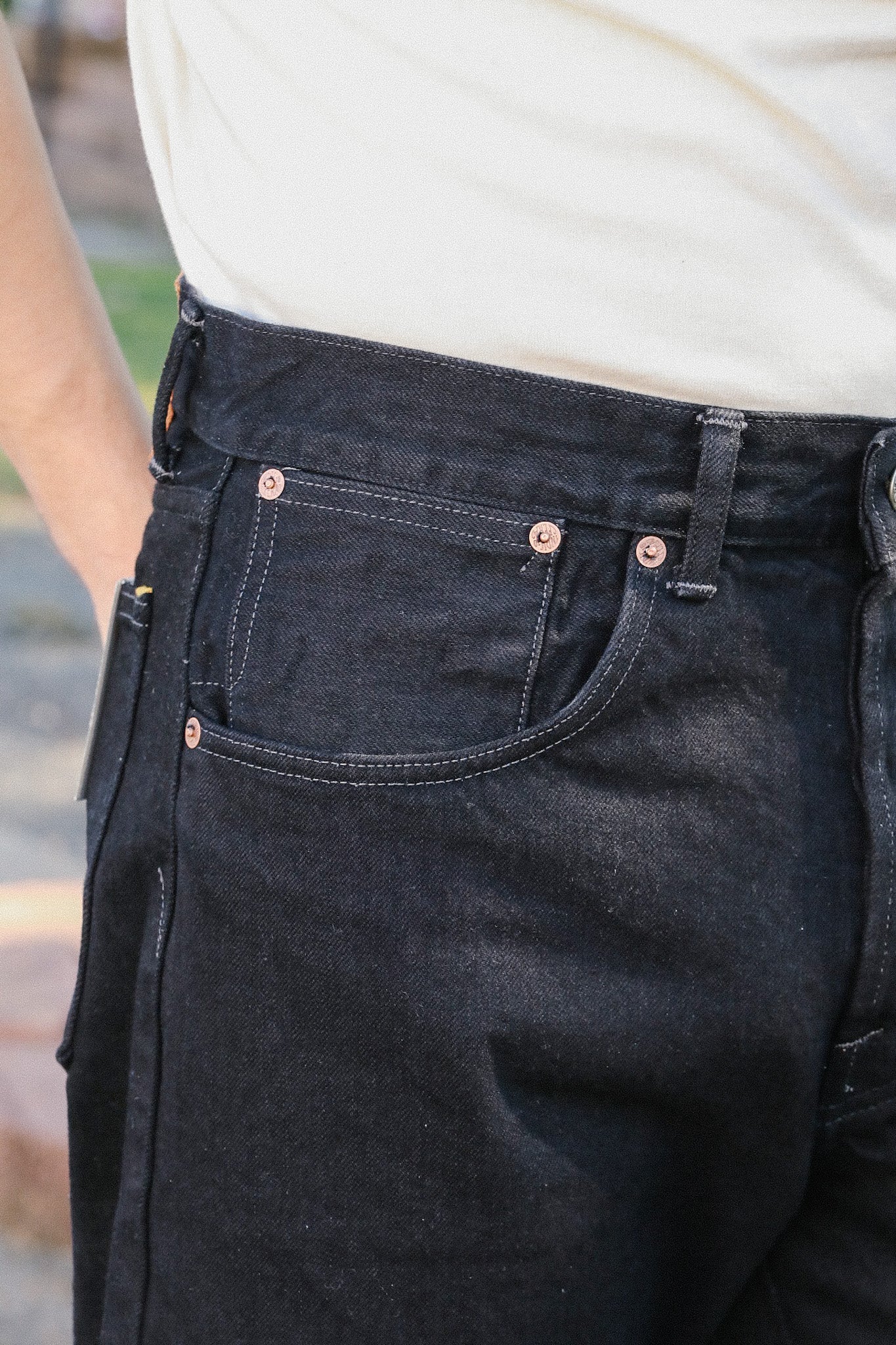 Close-up of black denim work pants with reinforced copper rivets and side tool pocket