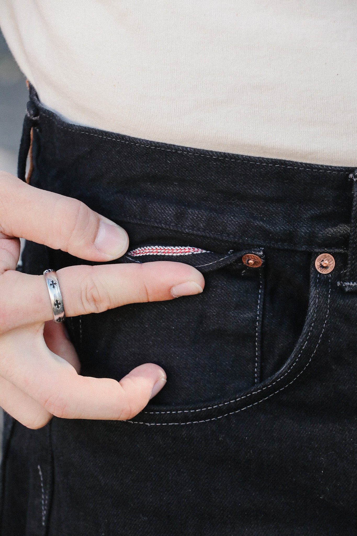 Hand with silver ring pointing at watch pocket inside black denim jeans with copper rivets