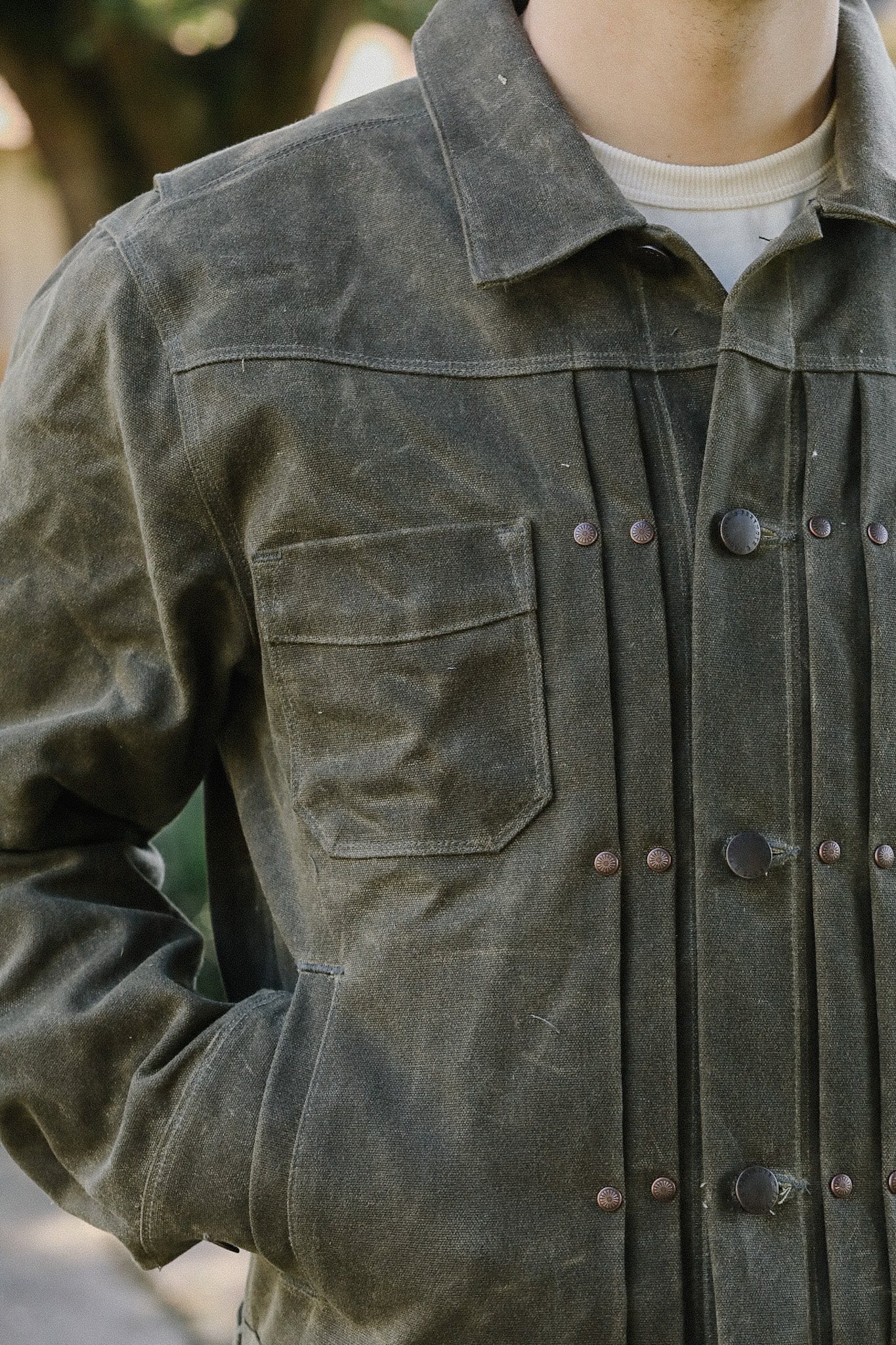 Close-up of person wearing green waxed canvas work jacket with multiple pockets and metal snaps at Iron Shop Provisions