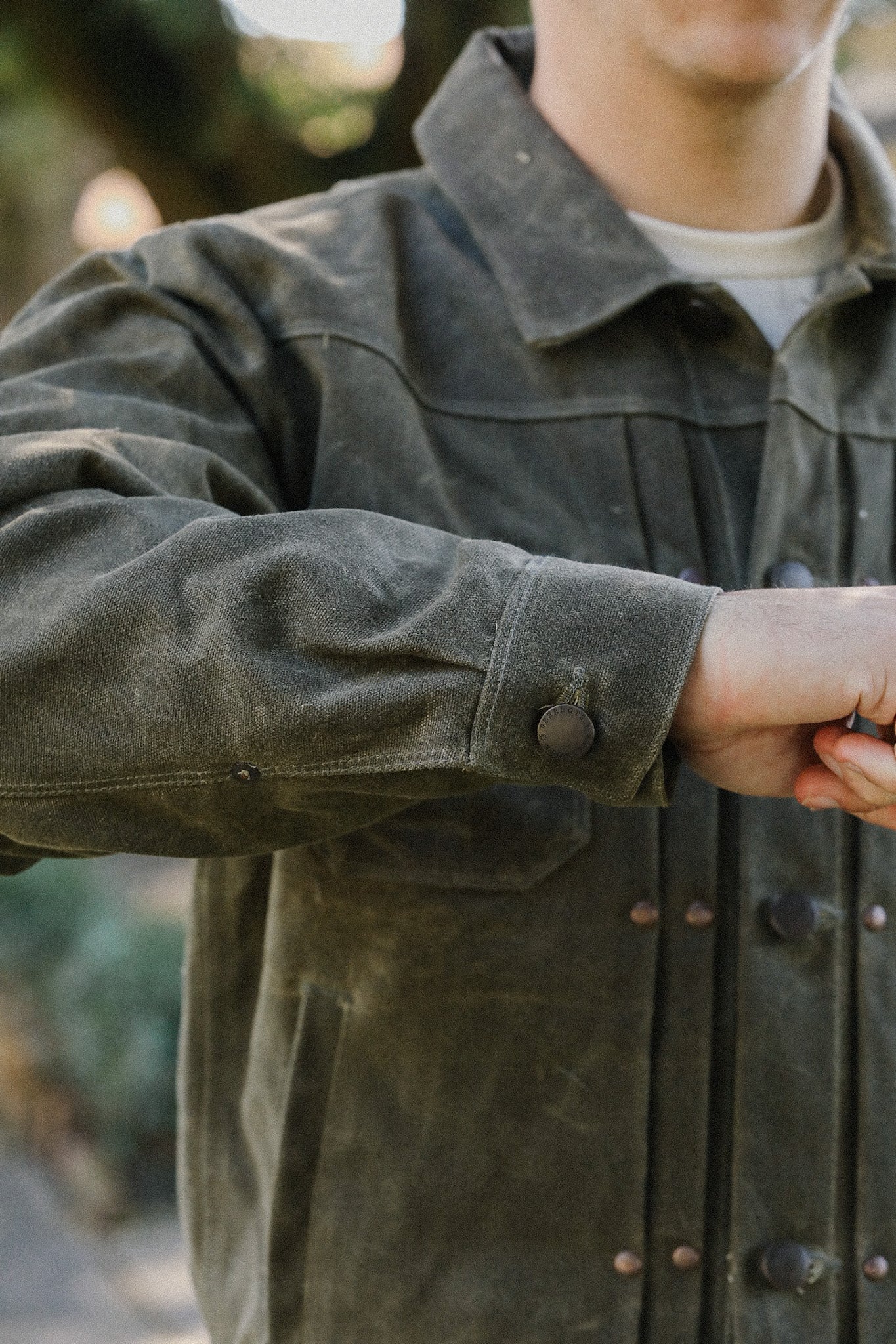 Close-up of a person wearing a rugged olive green work jacket from Iron Shop Provisions outdoors