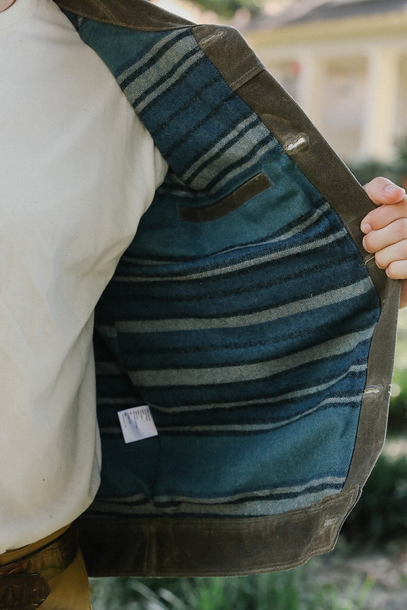 Close-up of hand holding open brown jacket revealing blue striped fabric lining inside
