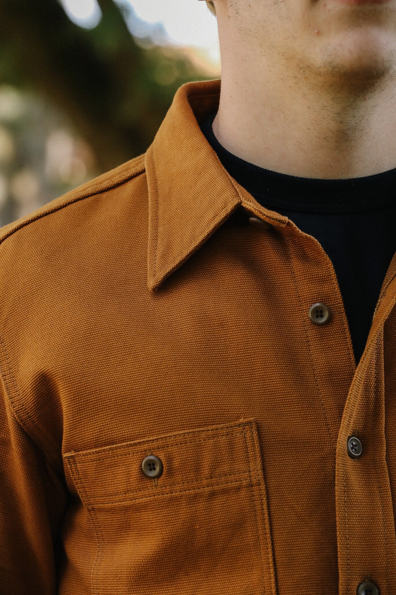 Close-up of a man wearing a brown heavy-duty canvas work jacket with buttons and a chest pocket