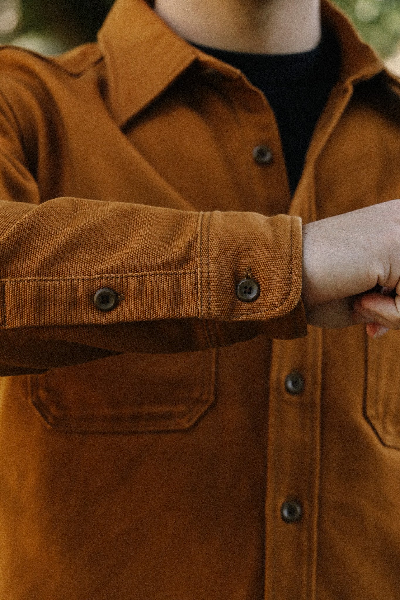 Close-up of a person wearing a brown button-up work shirt with textured fabric and front pockets