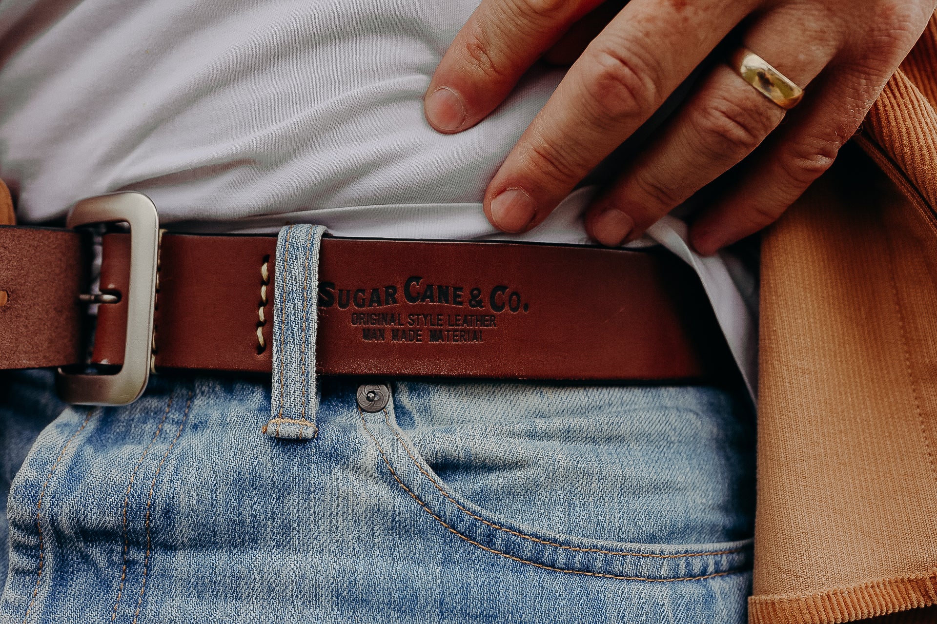 Close-up of brown Sugar Cane & Co. leather belt worn with light blue denim jeans and a white shirt