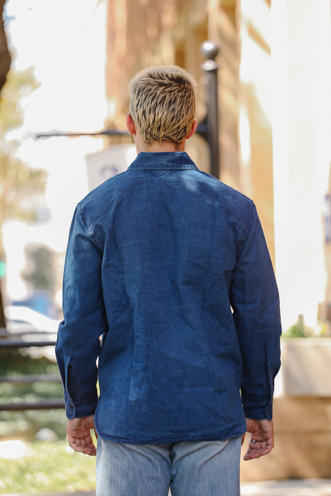 Man with blond hair wearing a blue denim jacket and light jeans walking outdoors