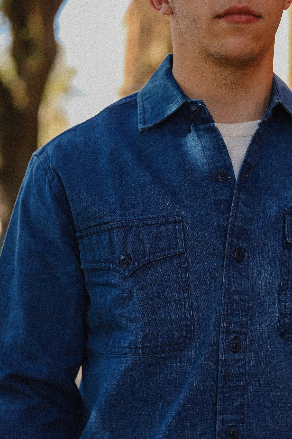 Close-up of a man wearing a blue denim button-up shirt with chest pockets outdoors